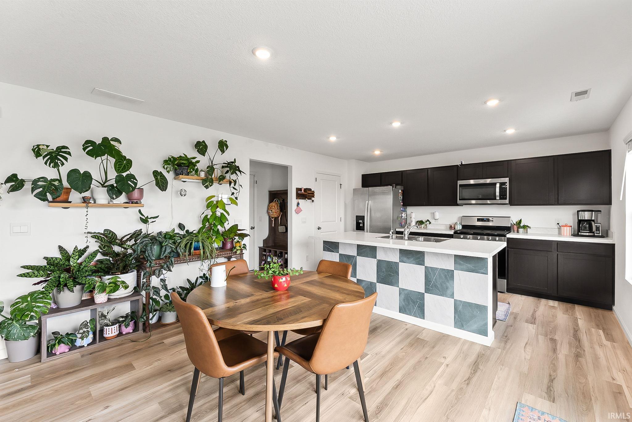 Modern kitchen featuring dark cabinetry, stainless steel appliances, a white countertop, and a checkered island with a solid surface counter