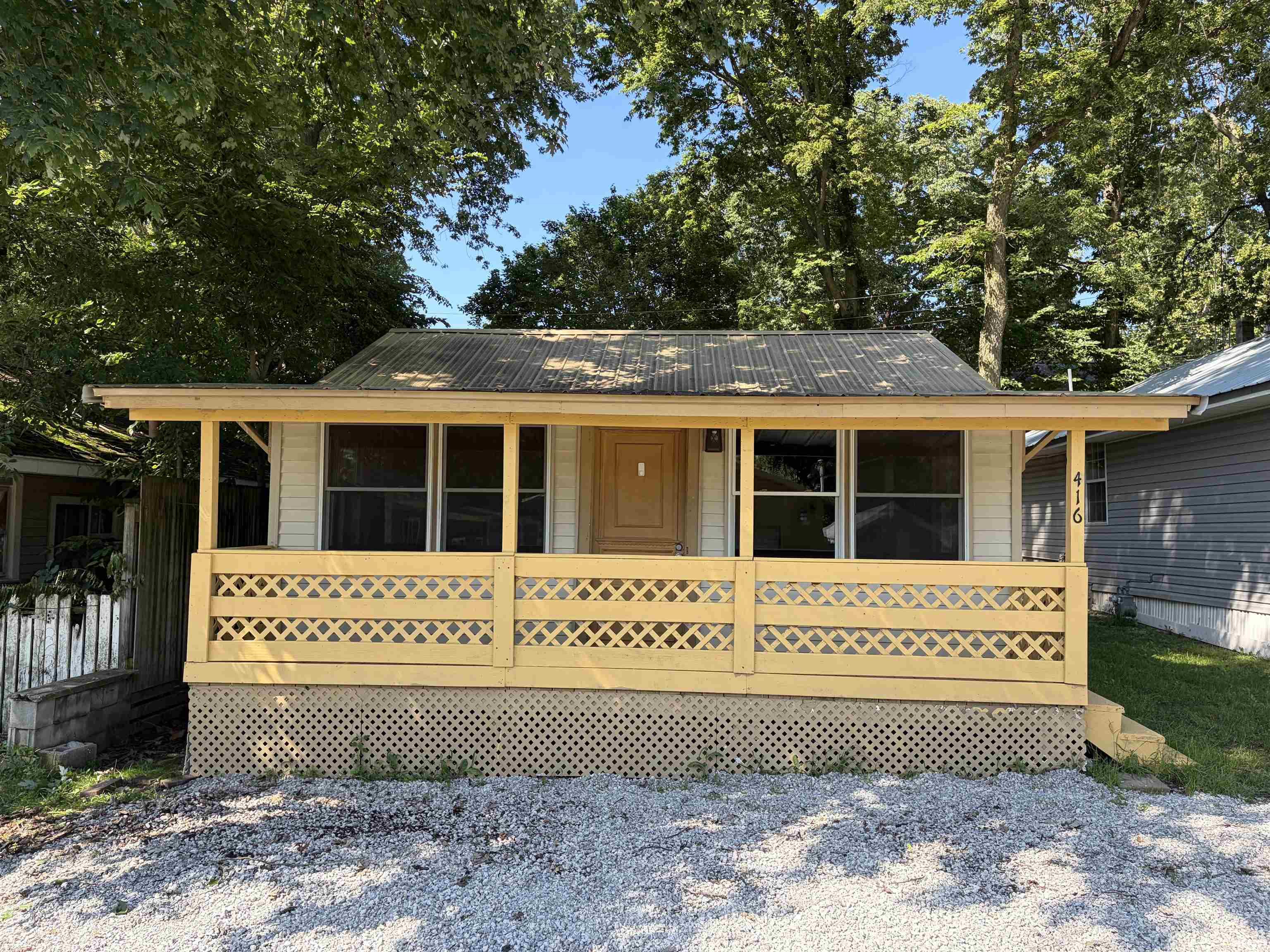 Front porch with lattice railing, white siding, and metal roof