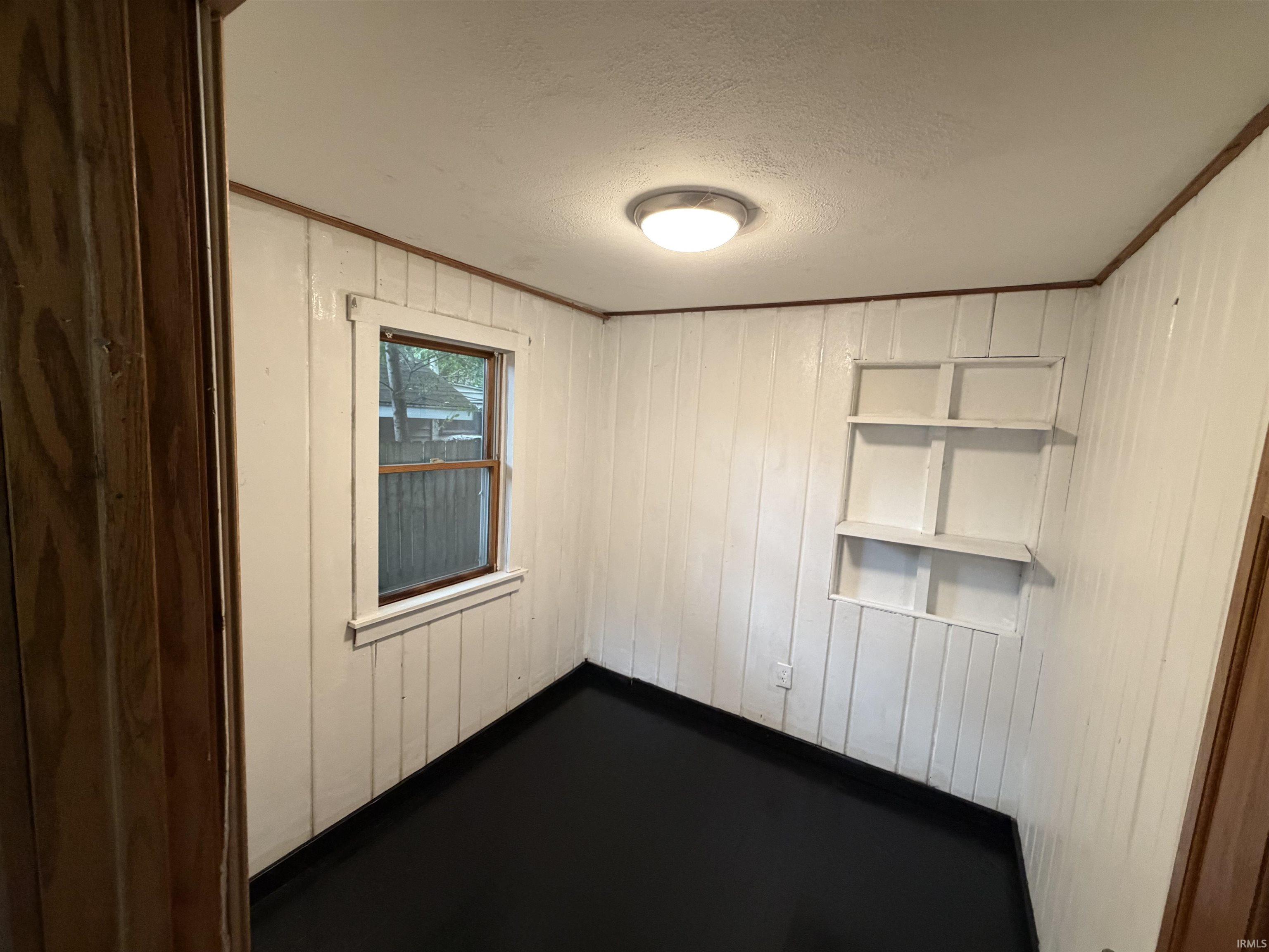 White vertical paneling, dark flooring, built-in shelving, single window, and flush mount ceiling light