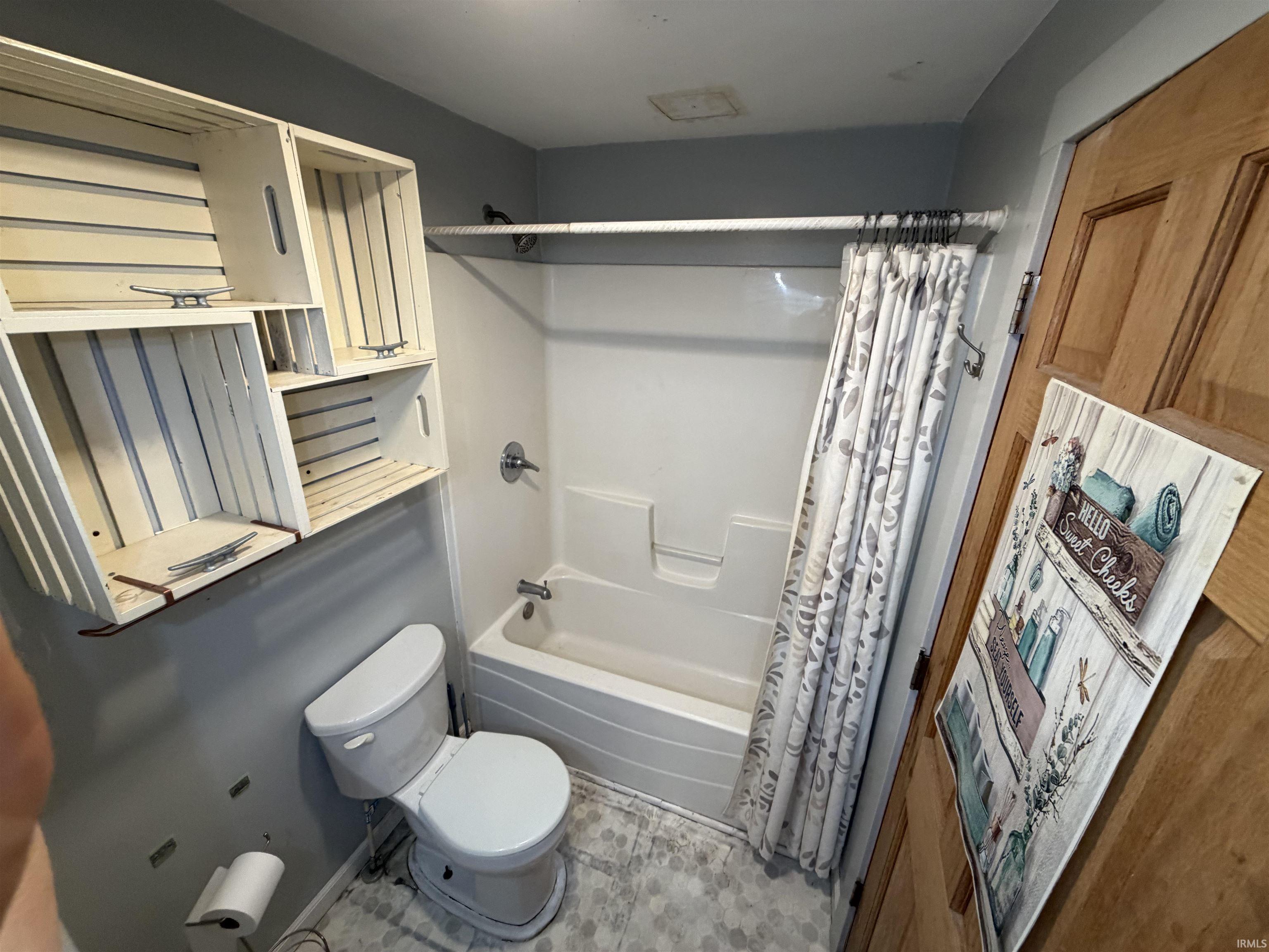 White bathtub with shower, white toilet, and hexagon tile flooring