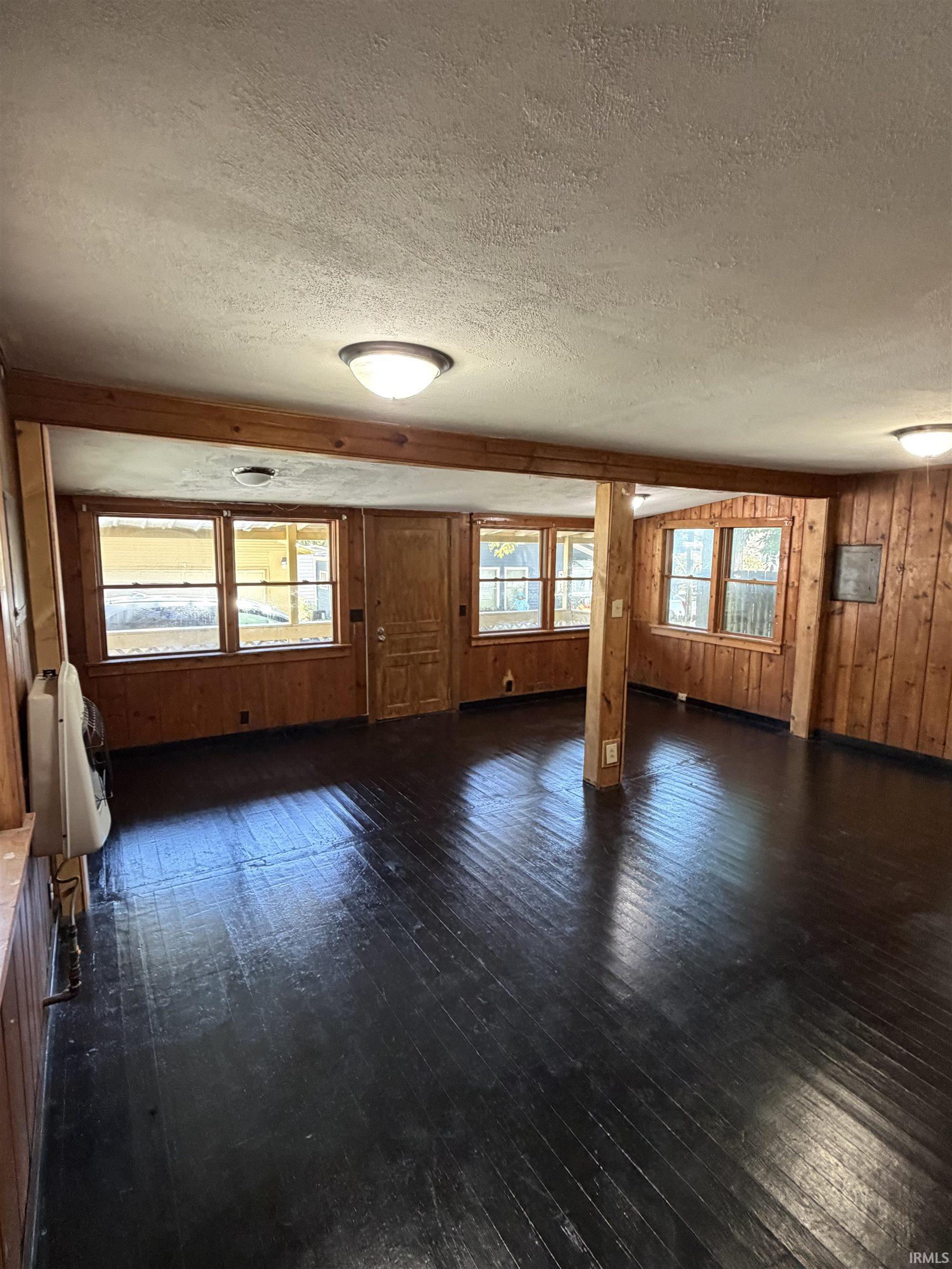 Dark wood-finish flooring, wood paneling, multiple windows, and ceiling-mounted light fixtures
