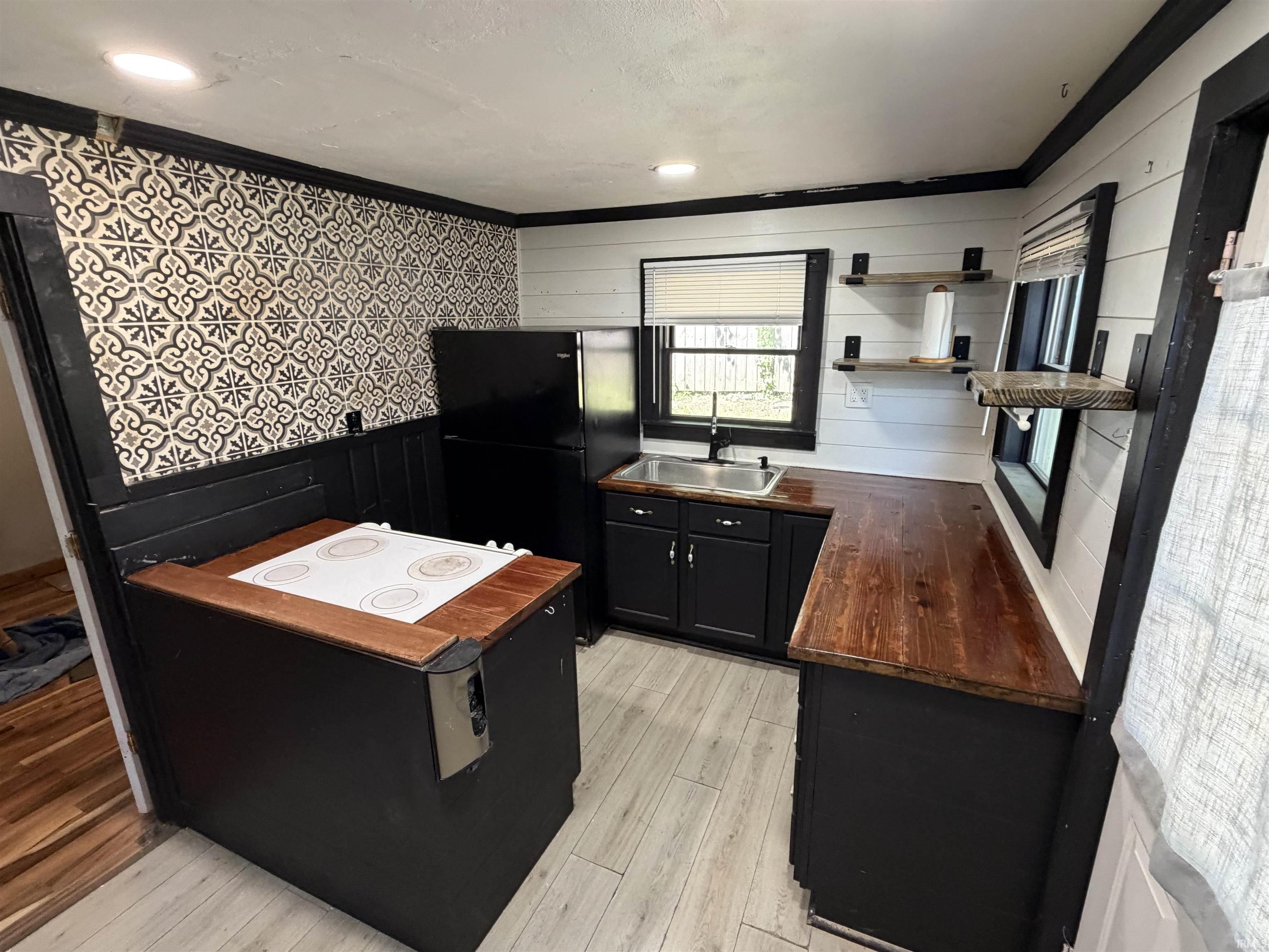 Kitchen featuring wood-finish countertops, black cabinetry, an integrated cooktop, a stainless steel sink, and wood-finish open shelving