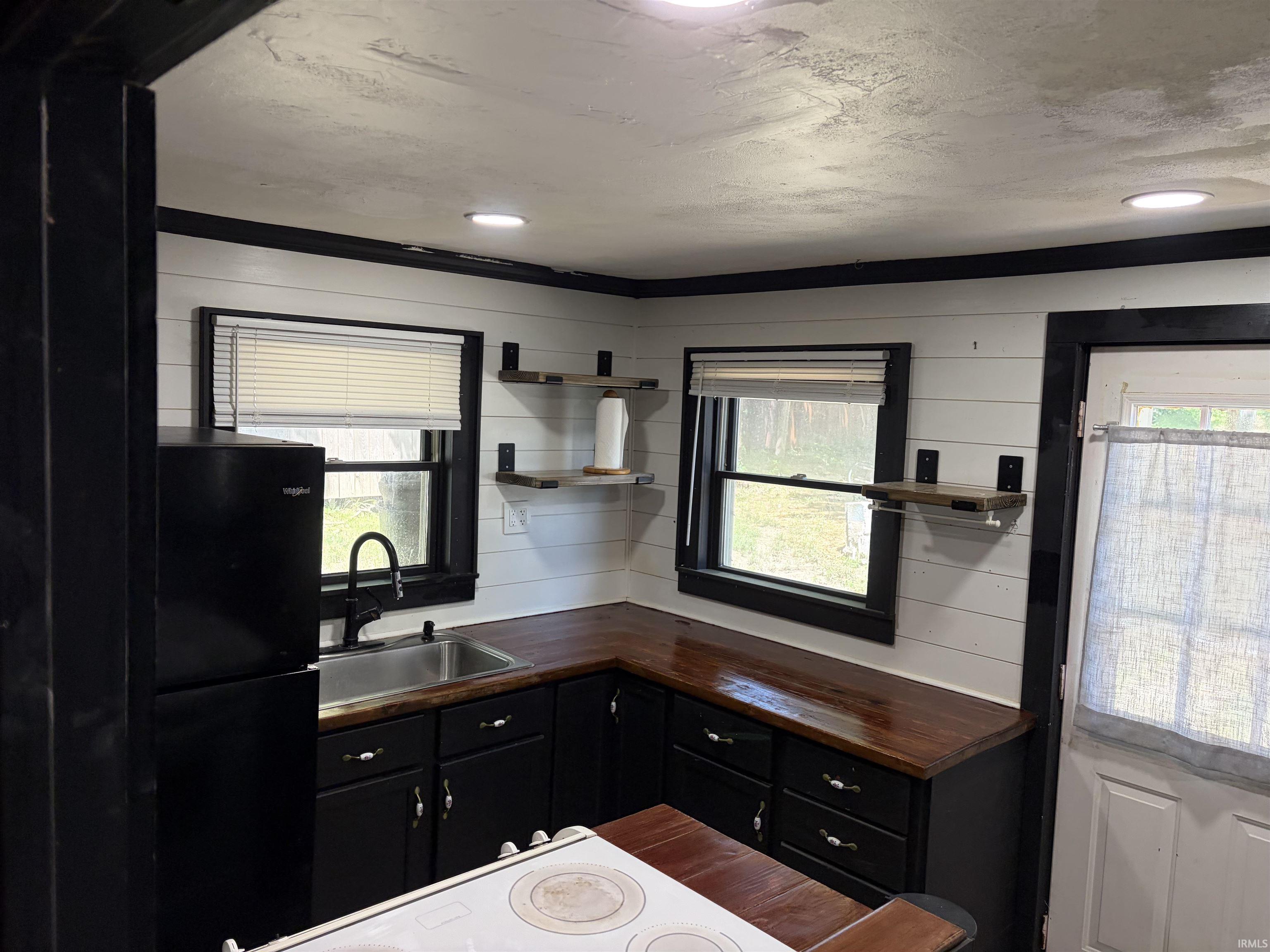 Kitchenette featuring black cabinetry, wood-finish countertops, stainless steel sink with a black gooseneck faucet, and integrated recessed lighting