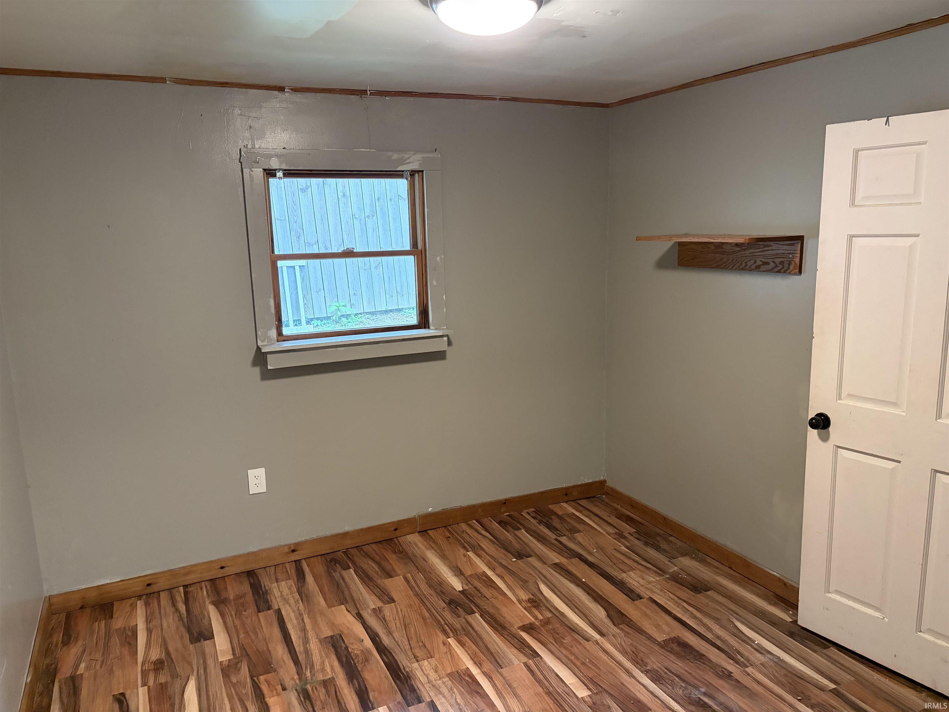Wood-finish flooring with coordinating wood trim, a single window, and a built-in wall shelf