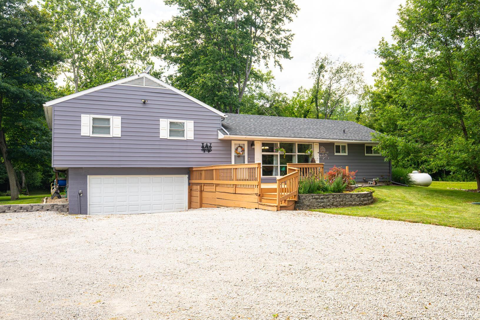 Multilevel exterior with siding, featuring a front deck with wood railing, a gravel driveway, and an integrated garage
