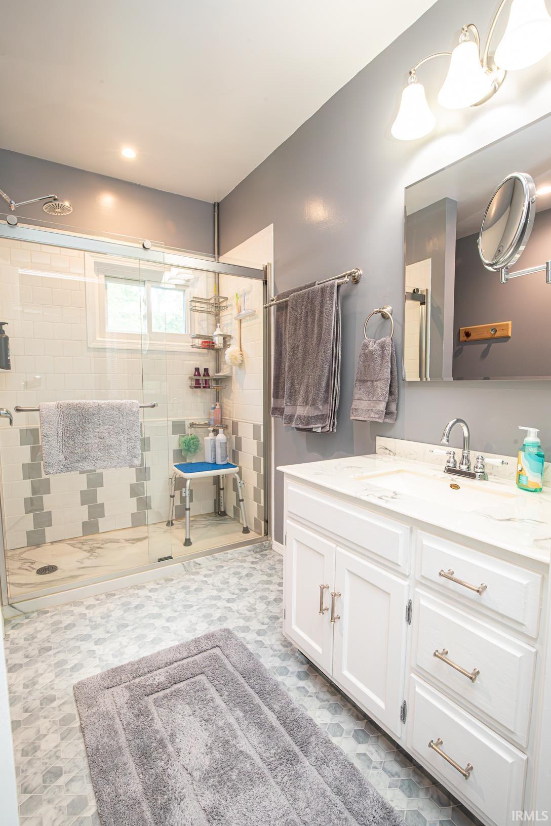 Bathroom featuring a glass-enclosed shower, white subway tile with a decorative accent band, and a single vanity with a white countertop