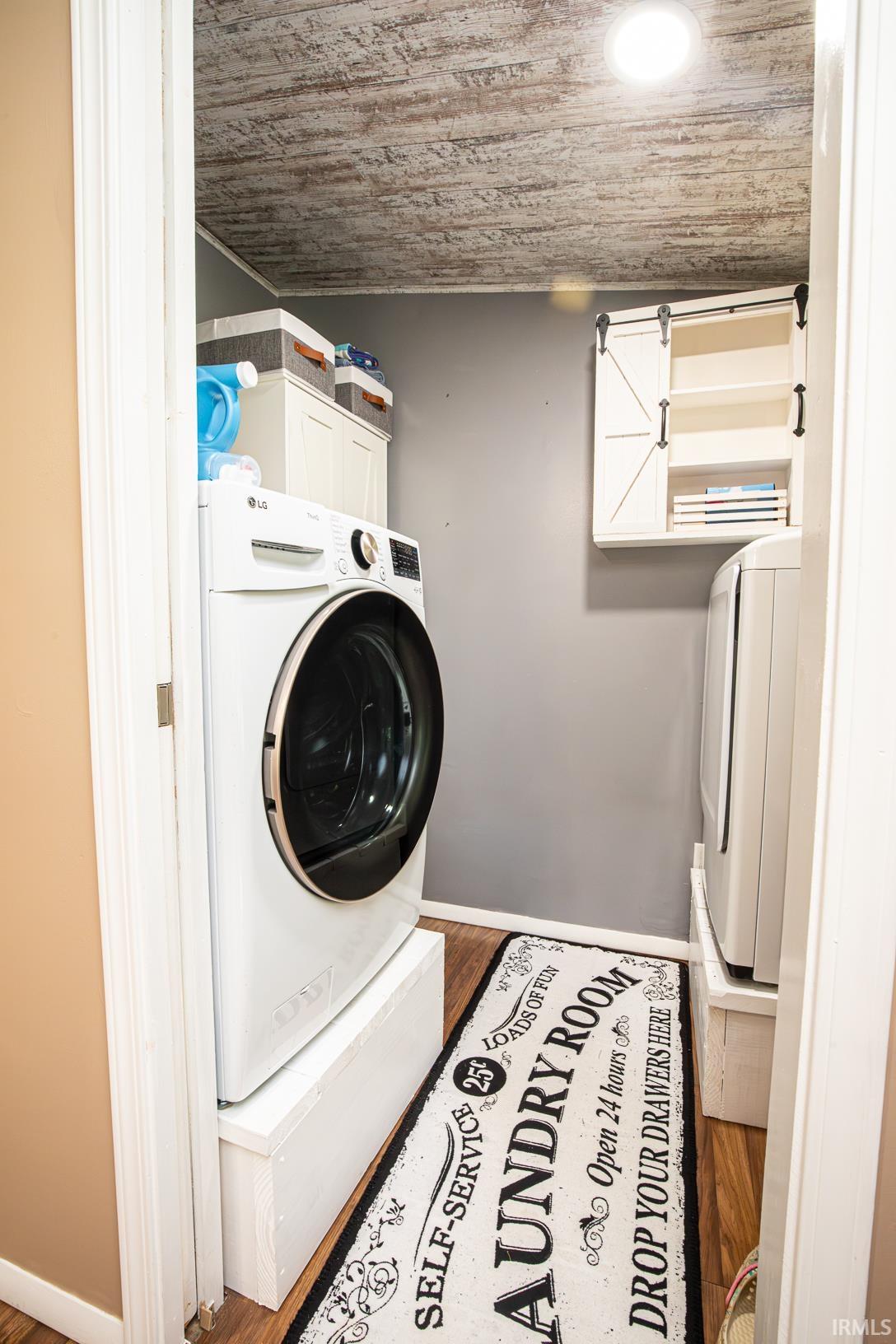 Dedicated laundry space featuring a textured ceiling, a front-load washer on a pedestal, and wood-finish flooring