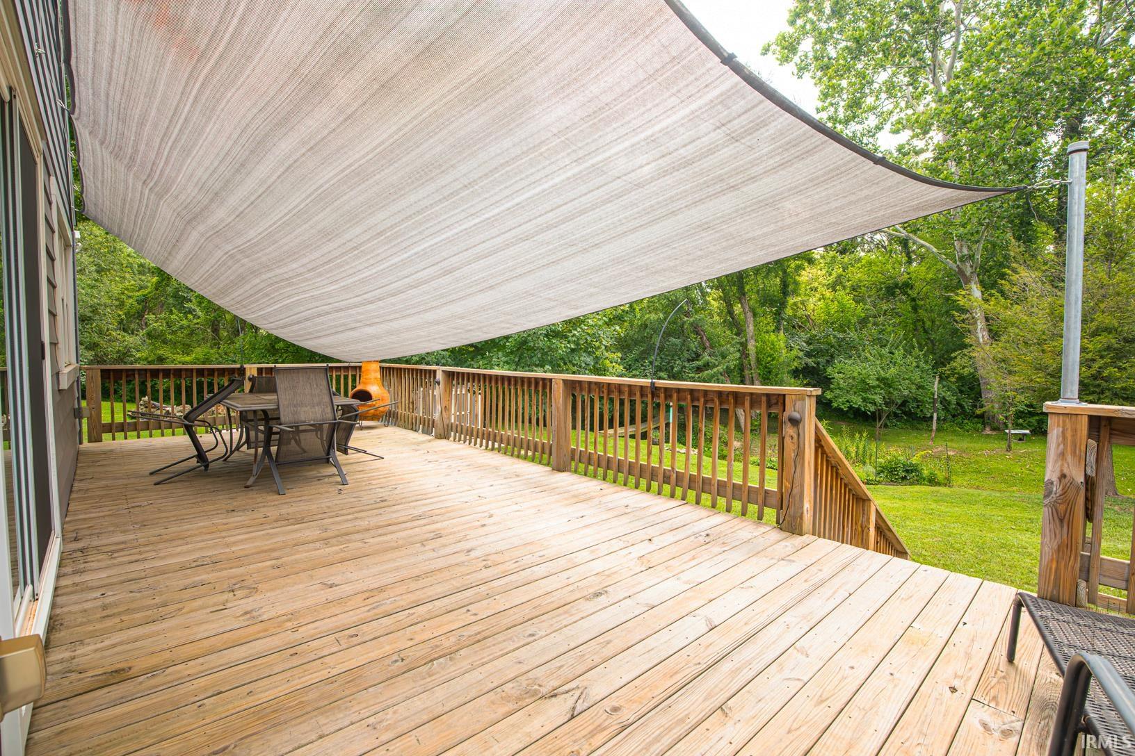 Expansive wood deck with a privacy screen overhead, featuring a wood railing system, integrated staircase, and direct access to a natural landscape with mature trees