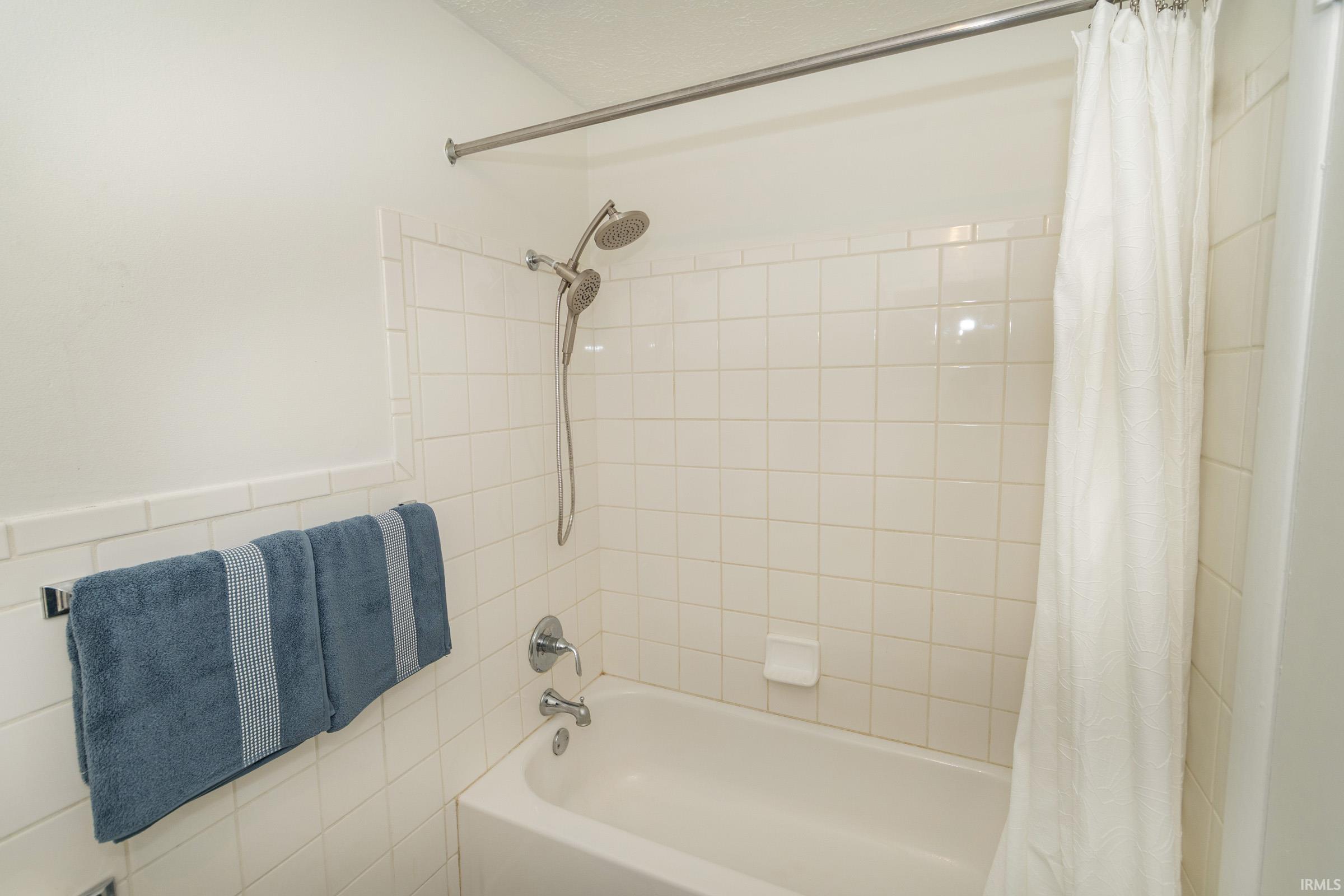 Clean and functional bathroom featuring white subway tile walls, a chrome shower head with adjustable hand spray, and a white porcelain bathtub with integrated tub spout