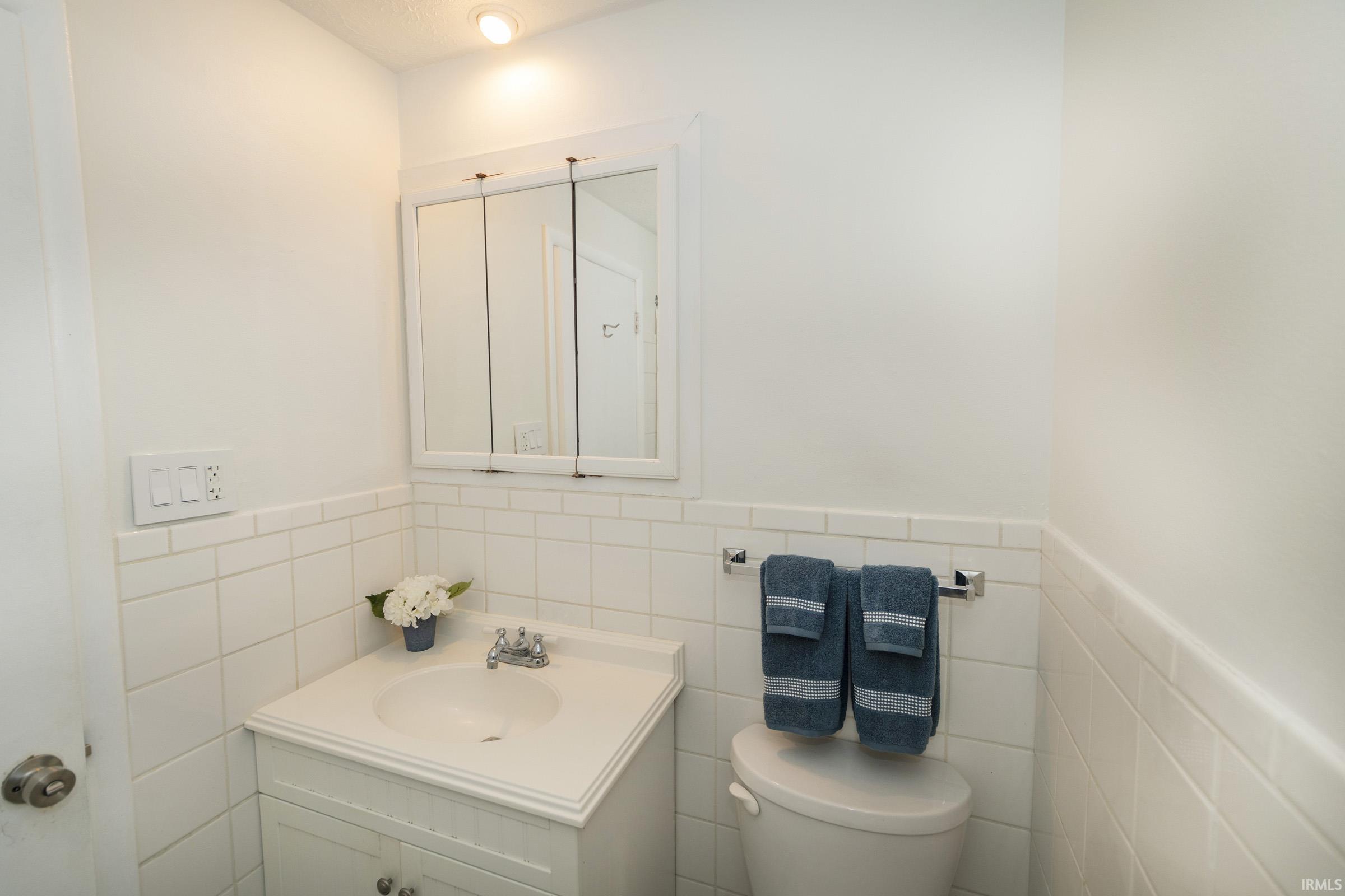 Clean and functional bathroom featuring white subway tile walls, a rectangular porcelain sink with chrome fixtures, a large medicine cabinet with mirrored doors, and chrome towel bar hardware