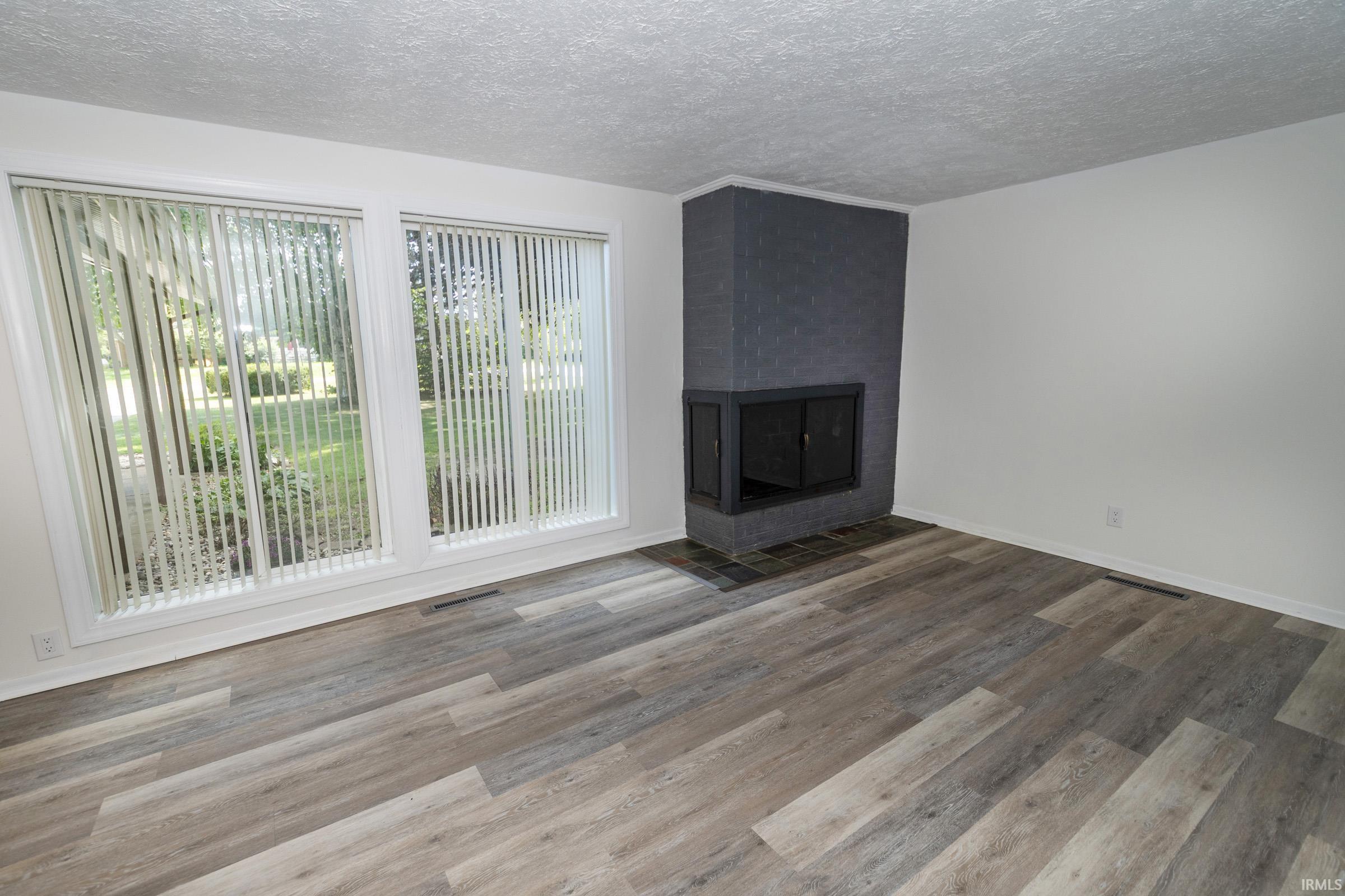 Spacious living area featuring wood-finish flooring throughout, expansive glass sliding doors with vertical blinds providing natural light, and a contemporary fireplace with dark surround and hearth