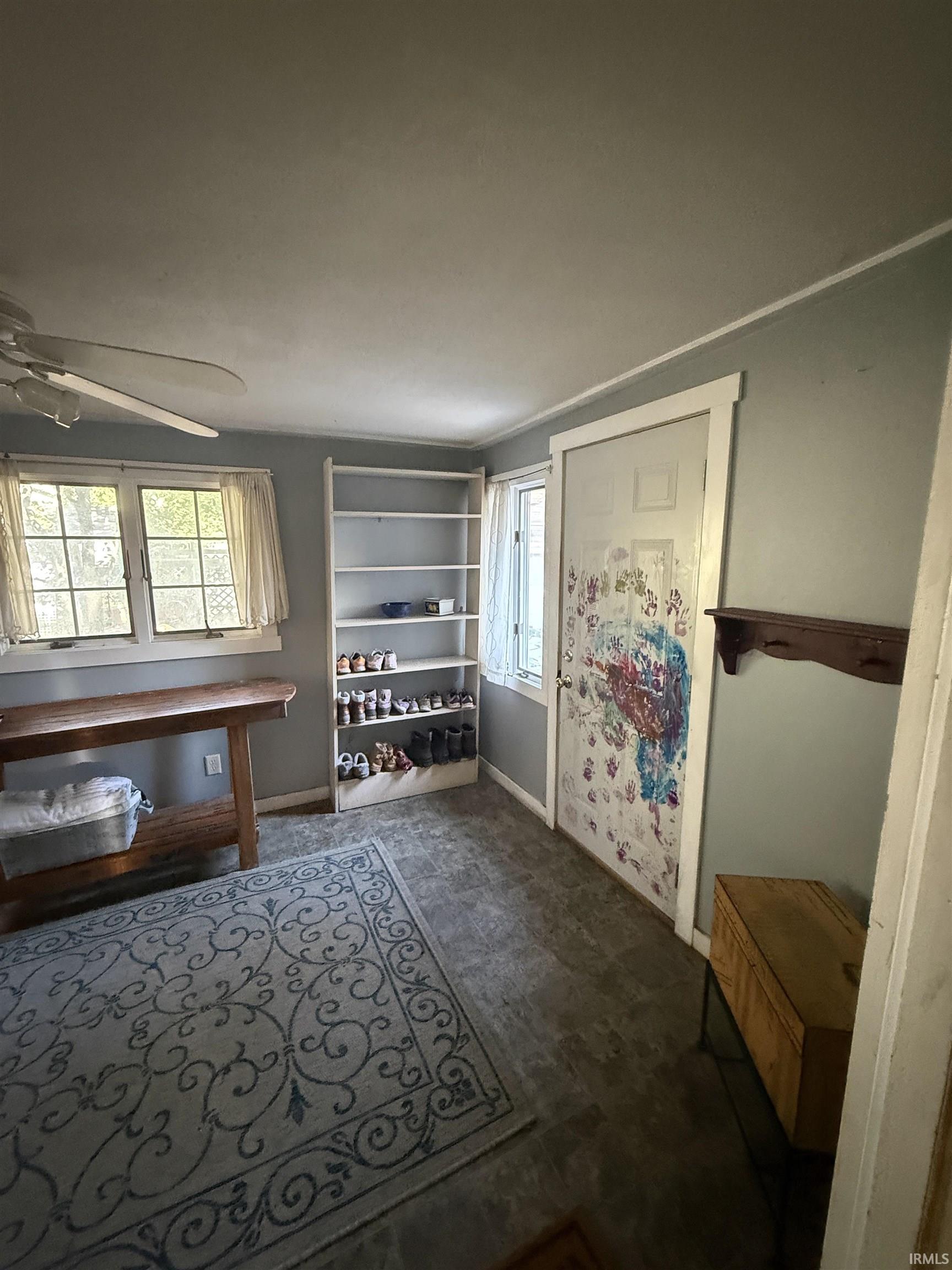 Ceiling fan with light fixture, multiple windows, built-in shelving, wood-finish flooring, and a solid door with trim