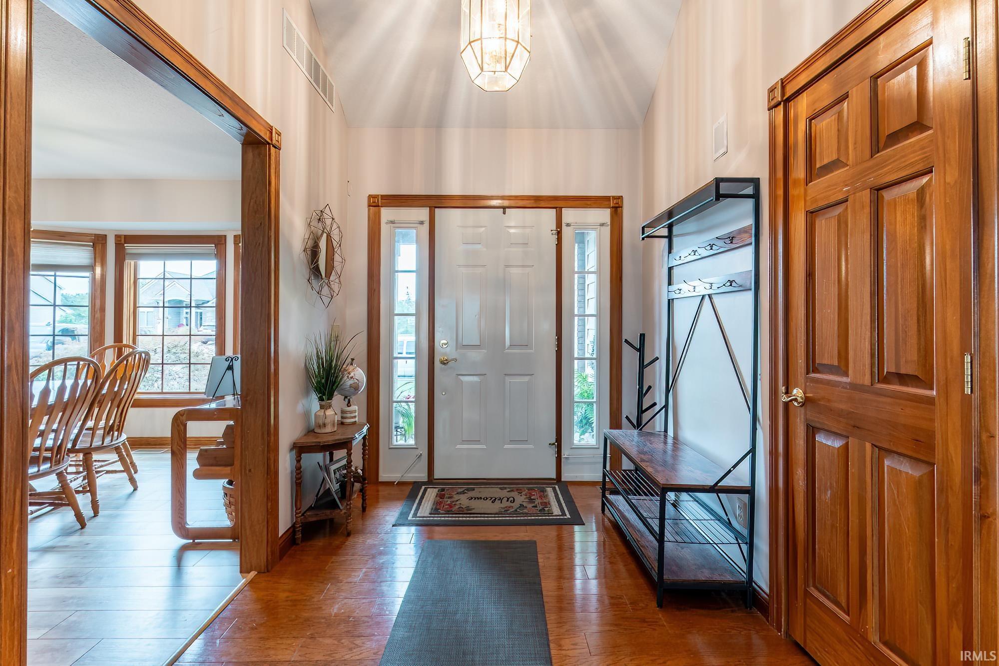 Vaulted ceiling entry with wood-finish flooring, white paneled front door with sidelights, and a wood paneled interior door
