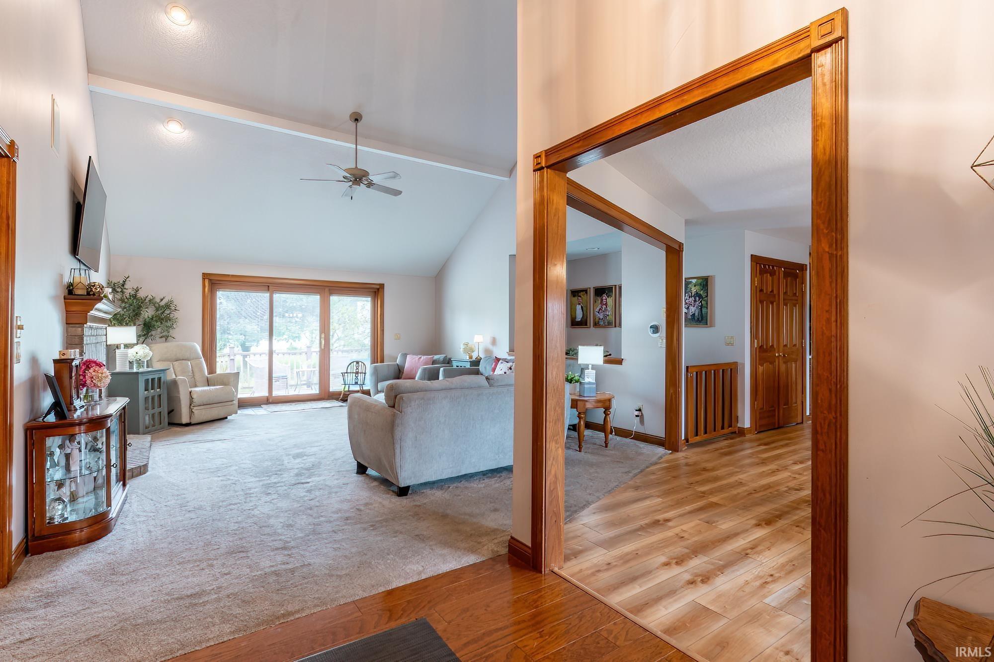 Vaulted ceiling with a ceiling fan, carpeted flooring, sliding glass doors, wood-finish flooring, and wood trim detailing