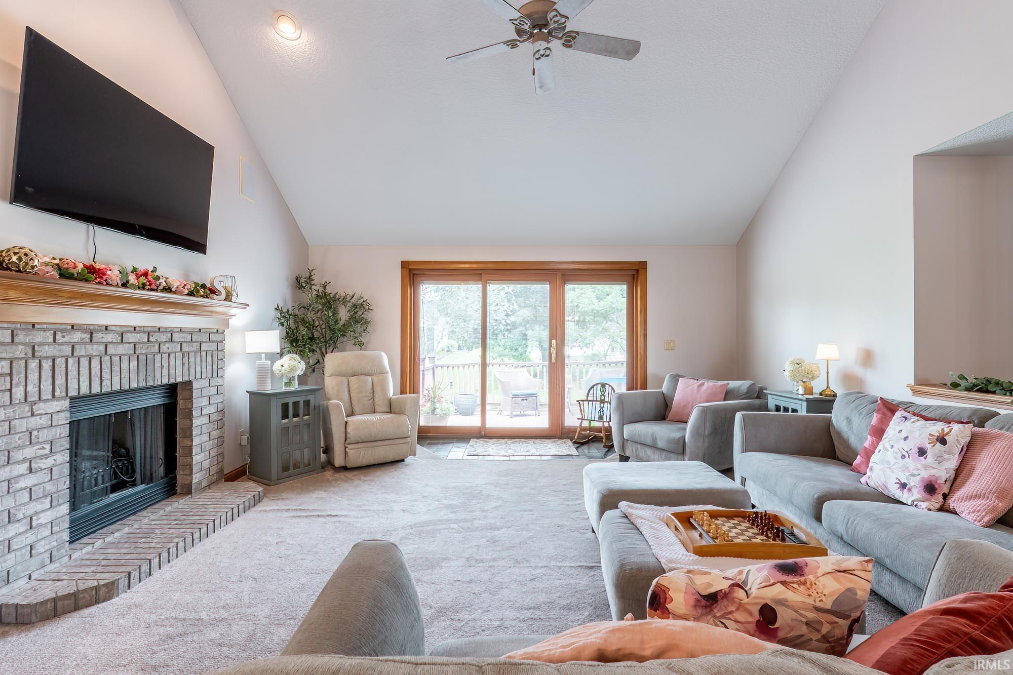 Vaulted ceiling with ceiling fan, brick fireplace, wood mantel, and sliding glass door