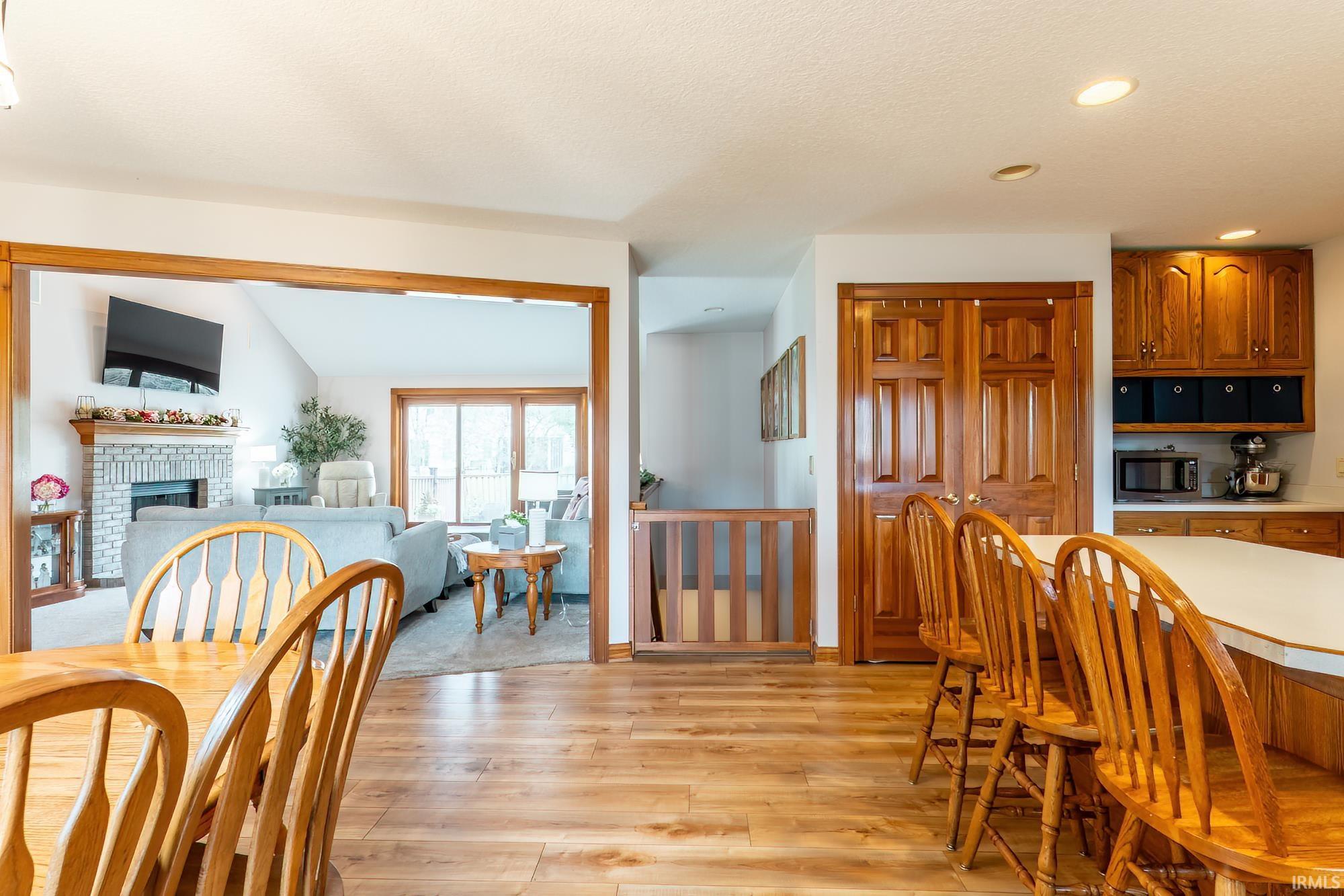 Wood-finish flooring throughout, kitchen with wood cabinetry and white countertops, living area with a stone-clad fireplace, and sliding glass doors