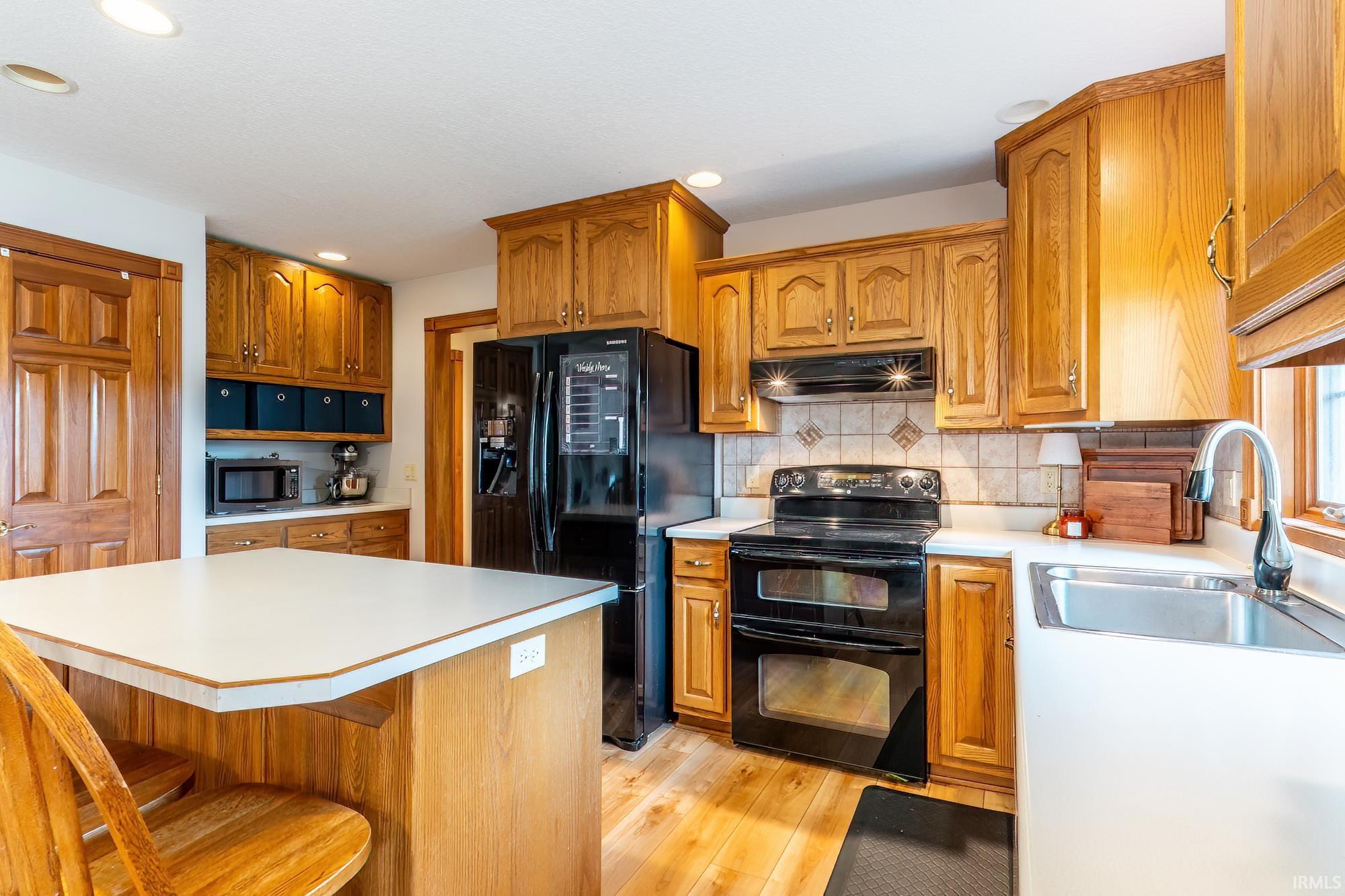 U-shaped kitchen featuring light wood cabinetry, a tiled backsplash, and recessed lighting