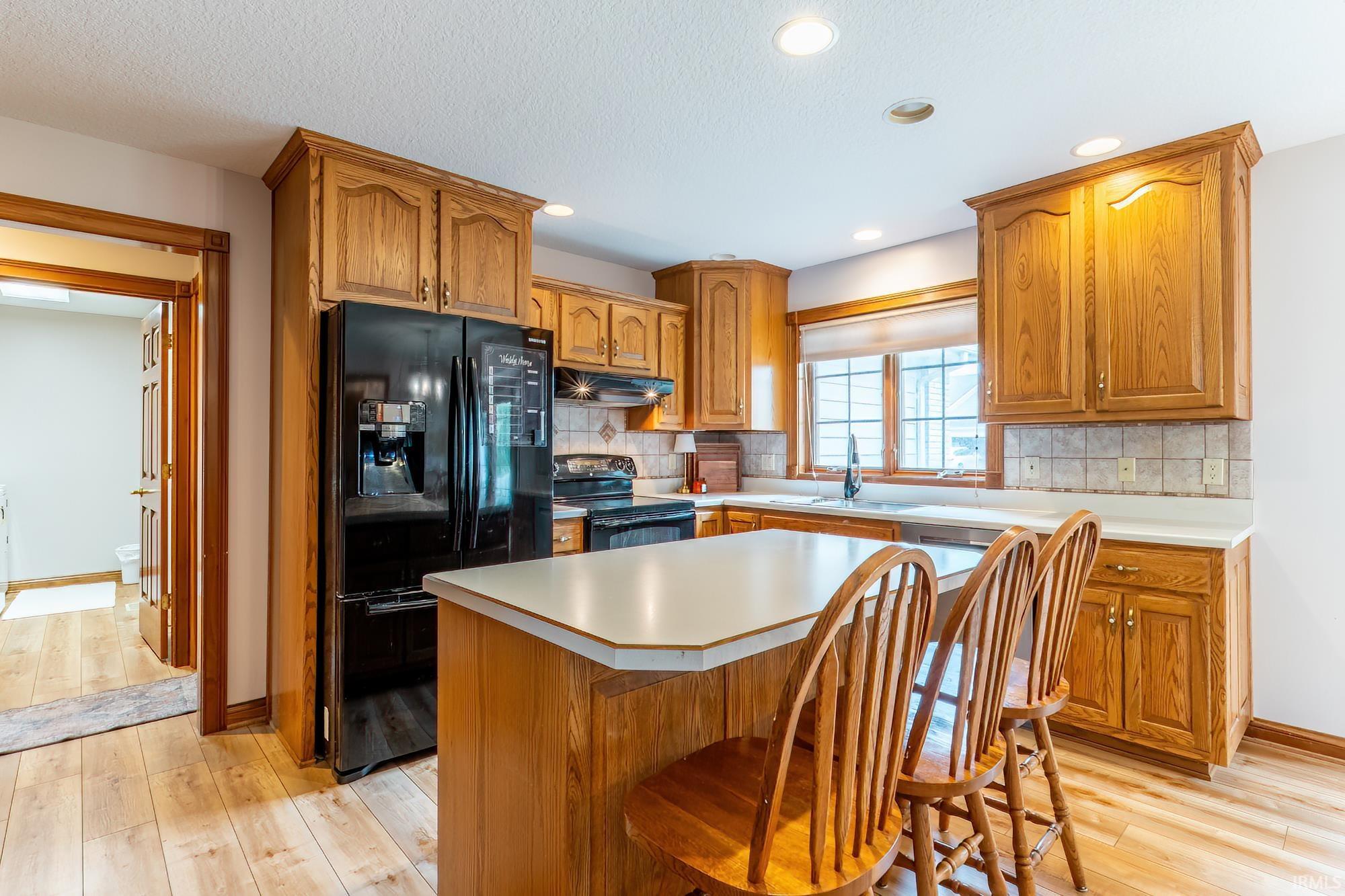 Kitchen with wood-finish flooring, wood cabinetry, white countertops, and black appliances