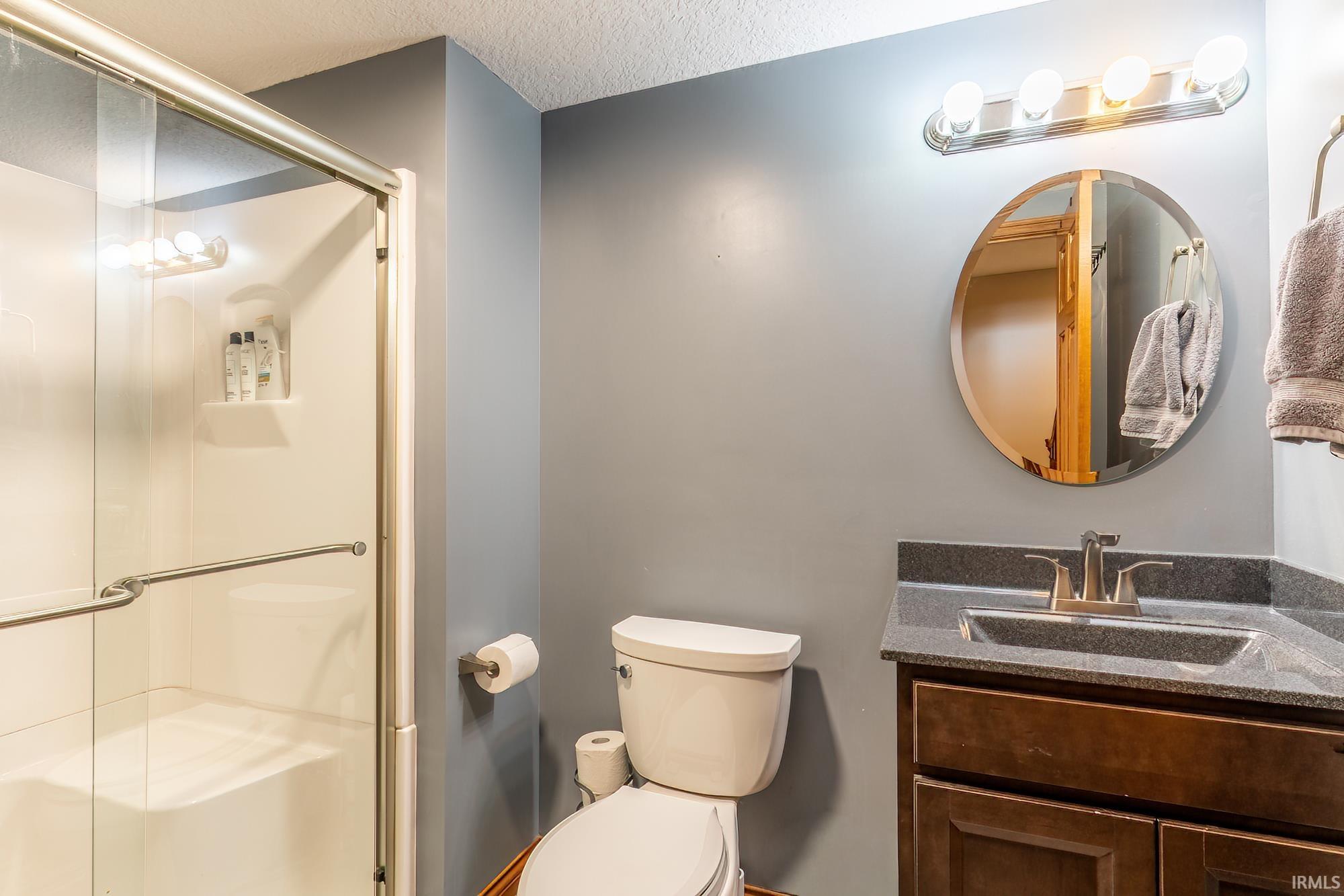 Built-in shower with sliding glass door, vanity with an integrated sink, dark cabinetry, and a circular mirror