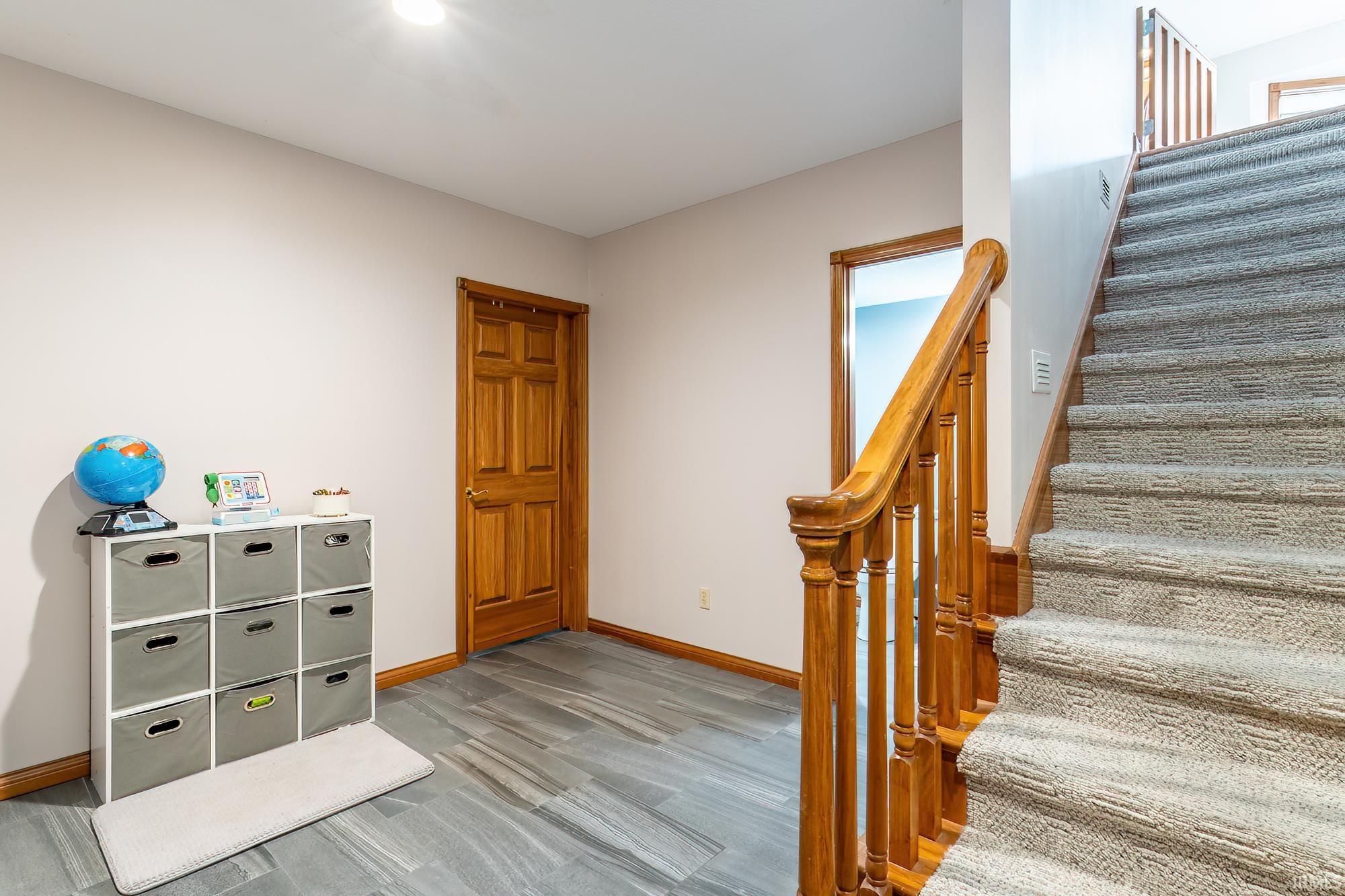 Carpeted staircase with wood-finish balusters and handrail, gray wood-finish flooring, and a wood-finish interior door