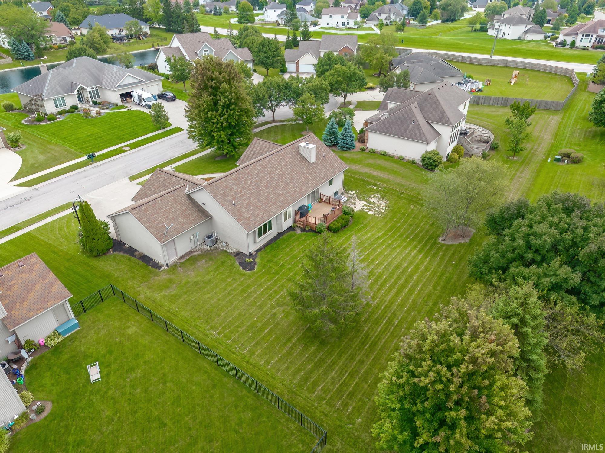 Expansive rear yard featuring a wood deck, mature trees, and a black metal fence