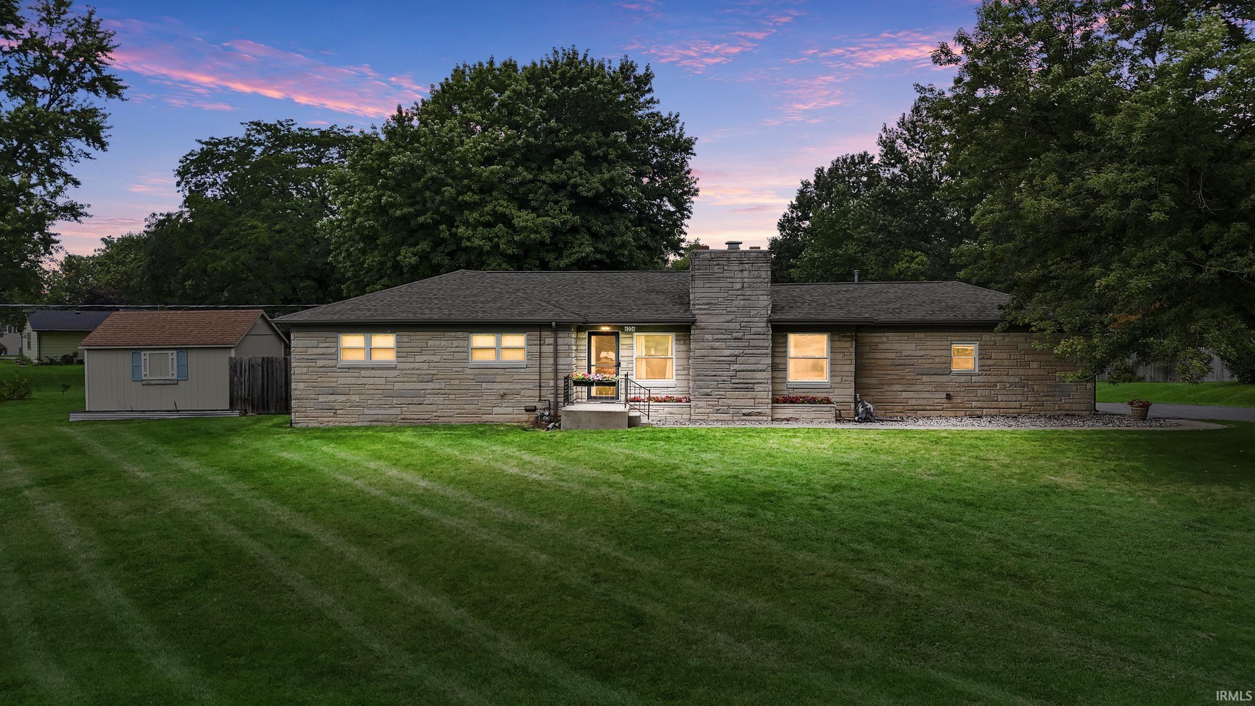 Stone exterior with a prominent chimney feature, dark-shingle roofing, and a well-maintained lawn