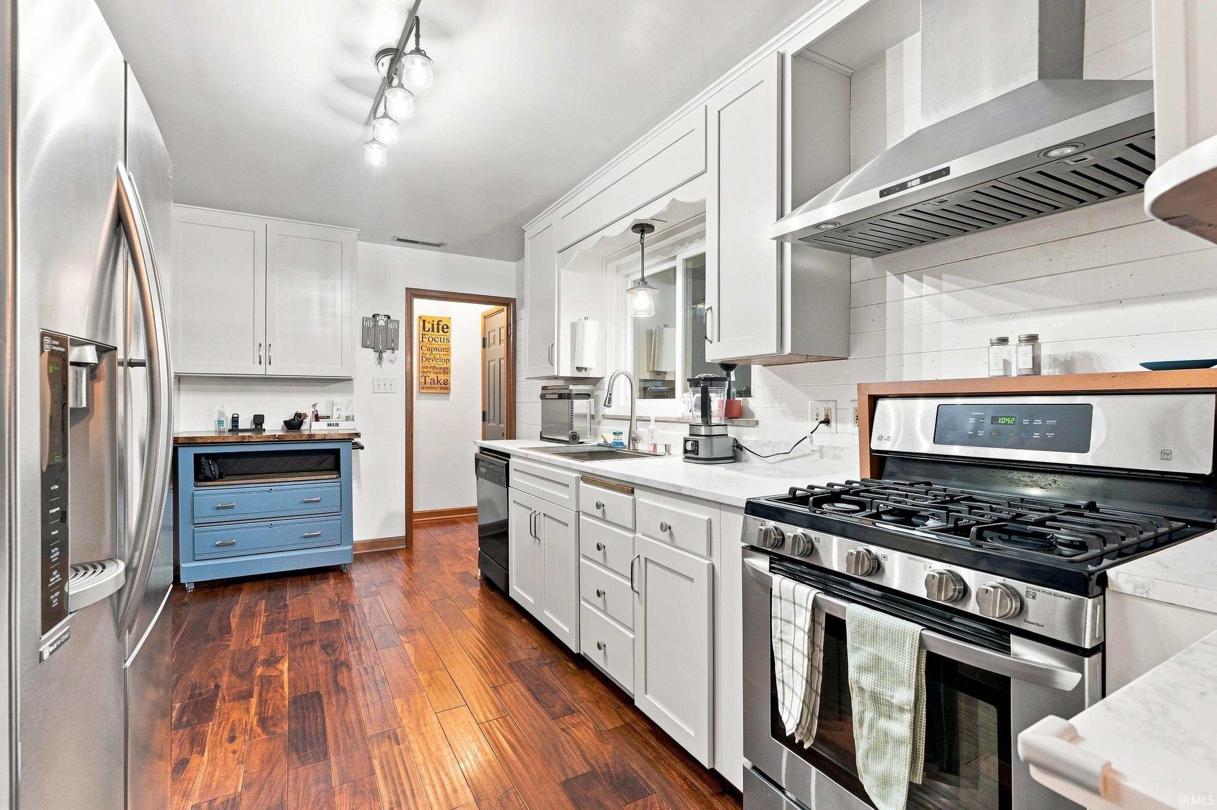 Kitchen featuring stainless steel appliances, white cabinetry, wood-finish flooring, white countertops, and a white shiplap-style backsplash