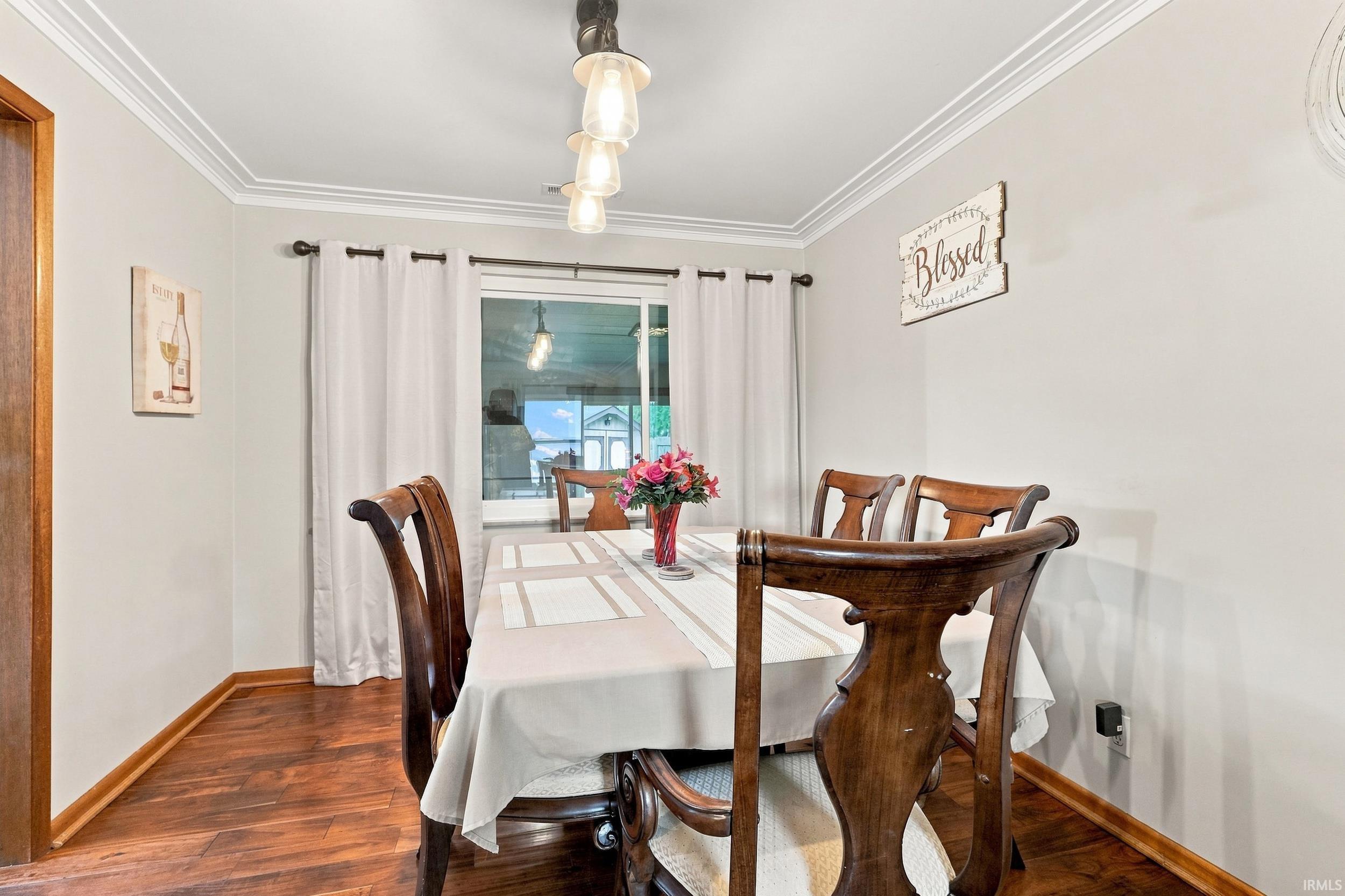 Wood-finish flooring, crown molding, and a multi-bulb pendant light fixture