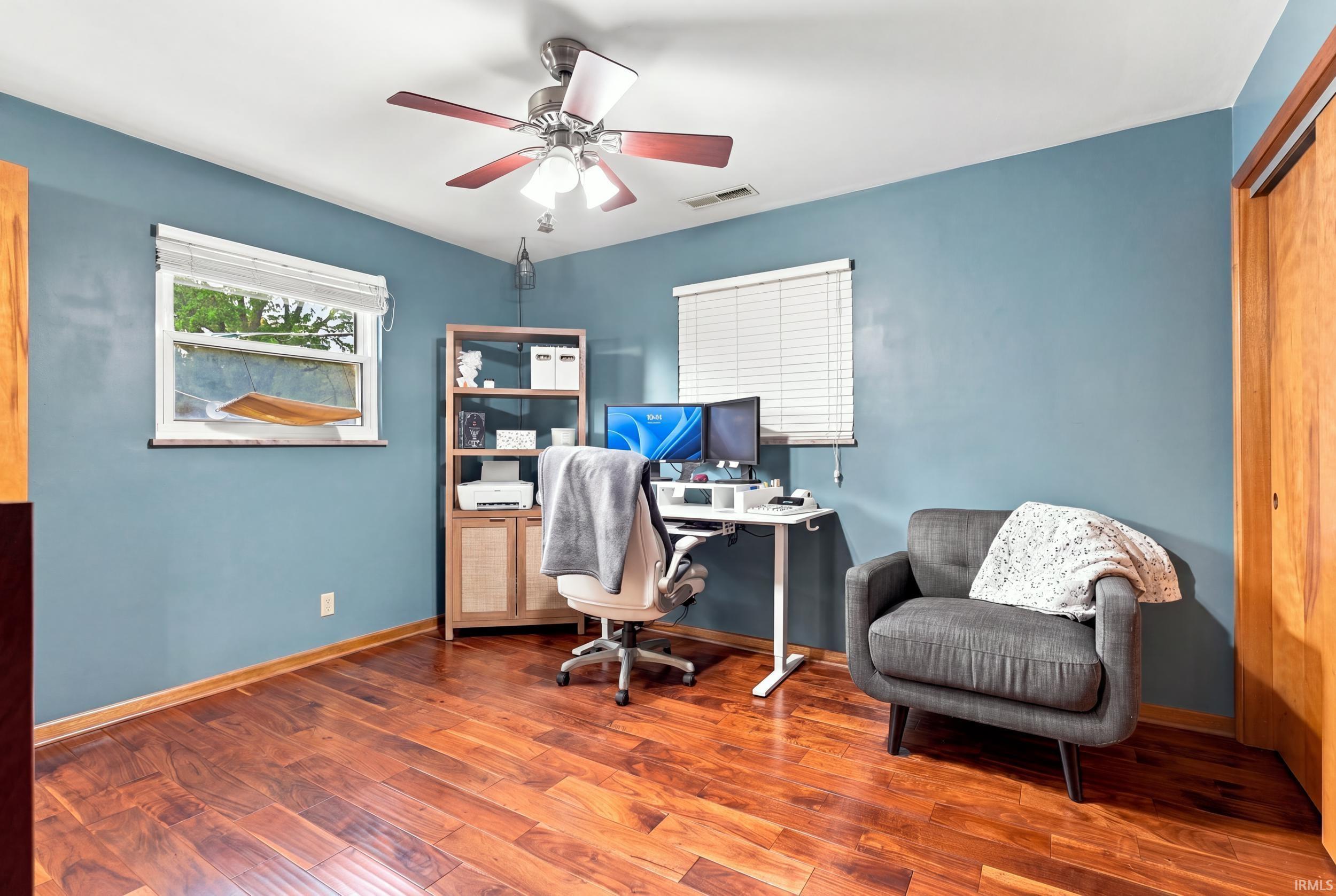 Wood-finish flooring, ceiling fan with integrated lighting, built-in shelving, and two windows with blinds