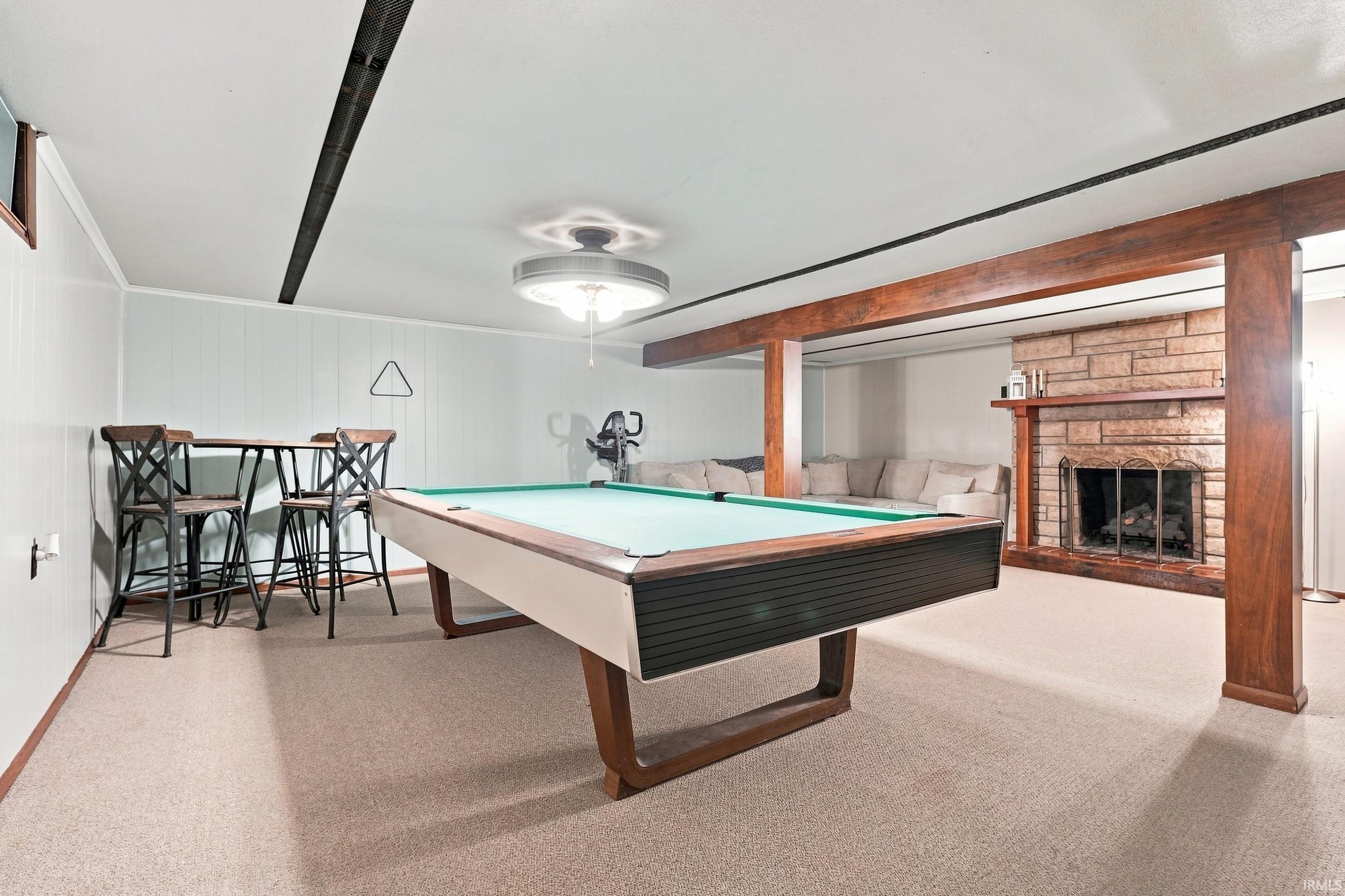 Carpeted flooring, paneled walls, exposed wood beams, and a stone-clad fireplace with a wood mantel