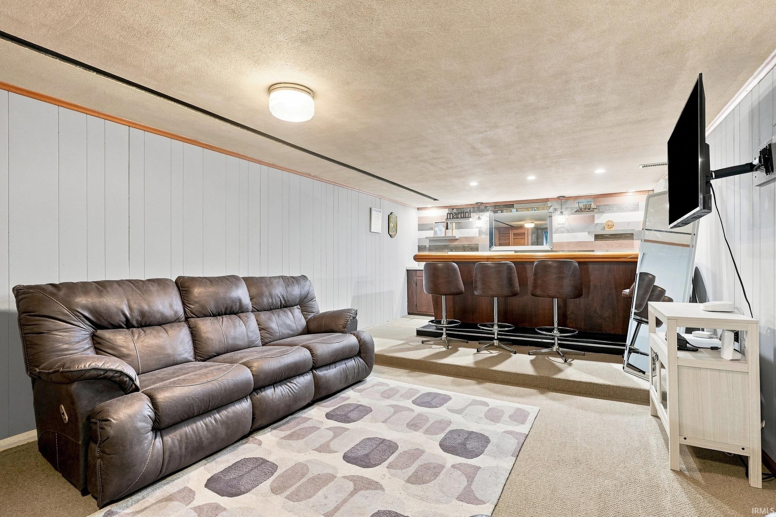 Integrated wet bar with barstool seating, recessed lighting, and wall-mounted television
