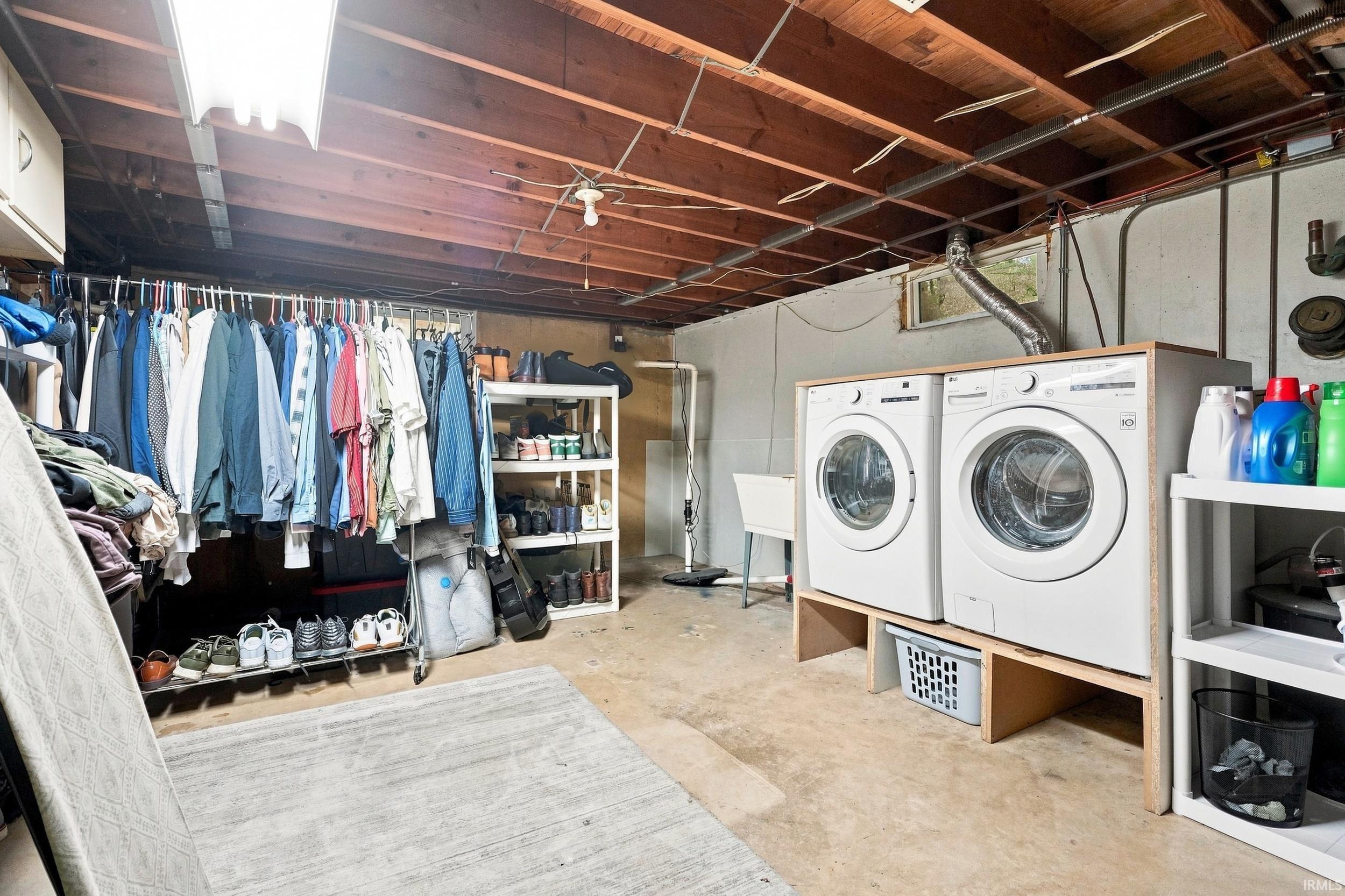 Exposed wood beam ceiling, concrete flooring, dual white front-load washing machines, utility sink, and overhead fluorescent lighting