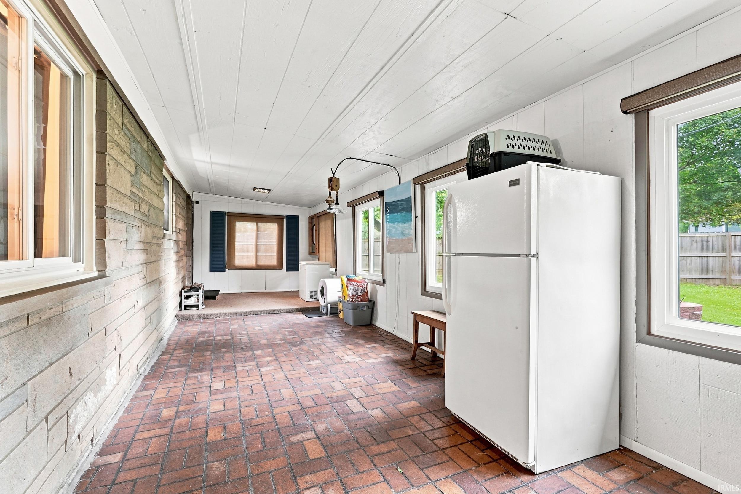 Enclosed patio featuring a brick flooring, white paneling, and a wood-paneled ceiling