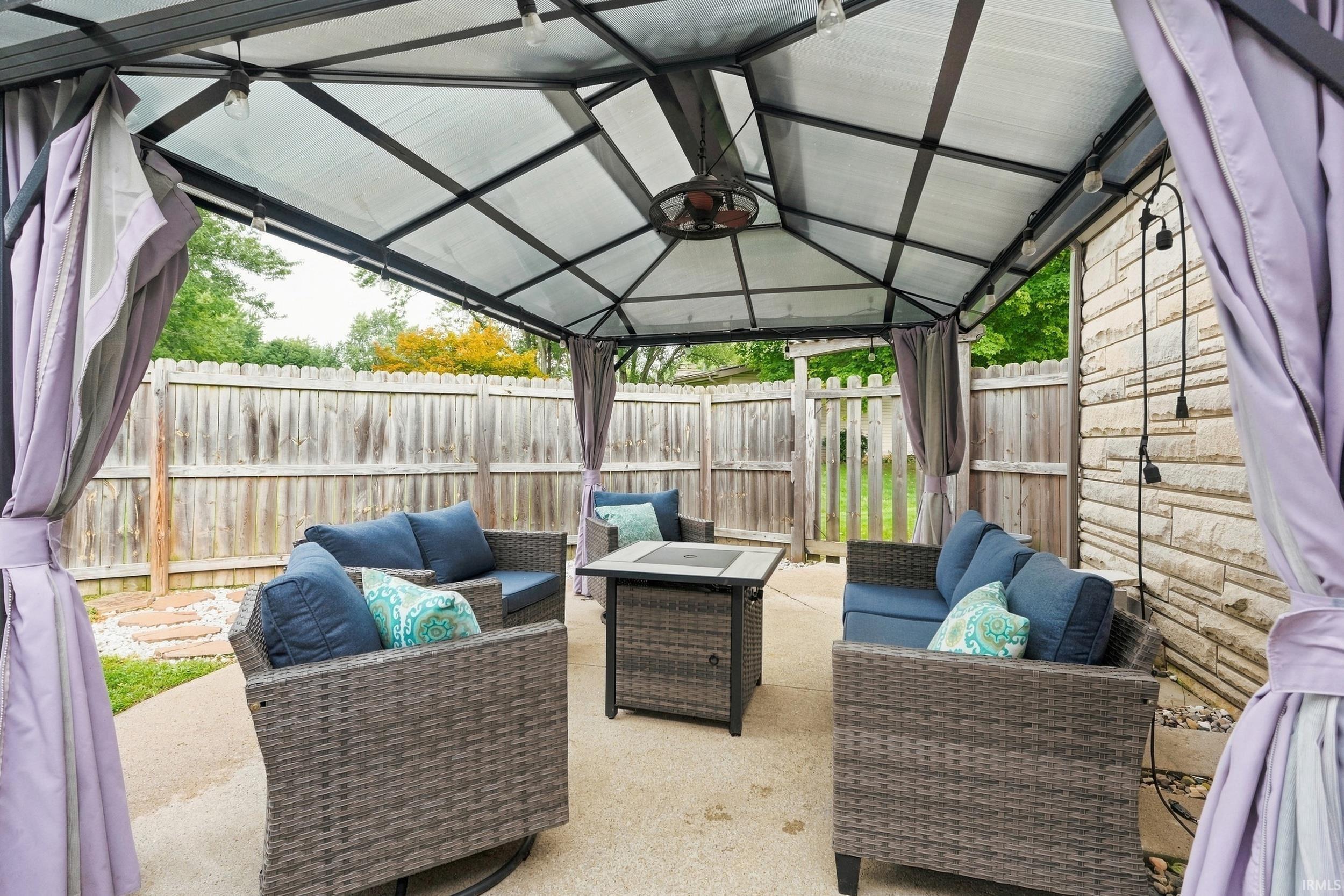 Outdoor covered patio with a built-in ceiling fan, string lighting, and a privacy fence