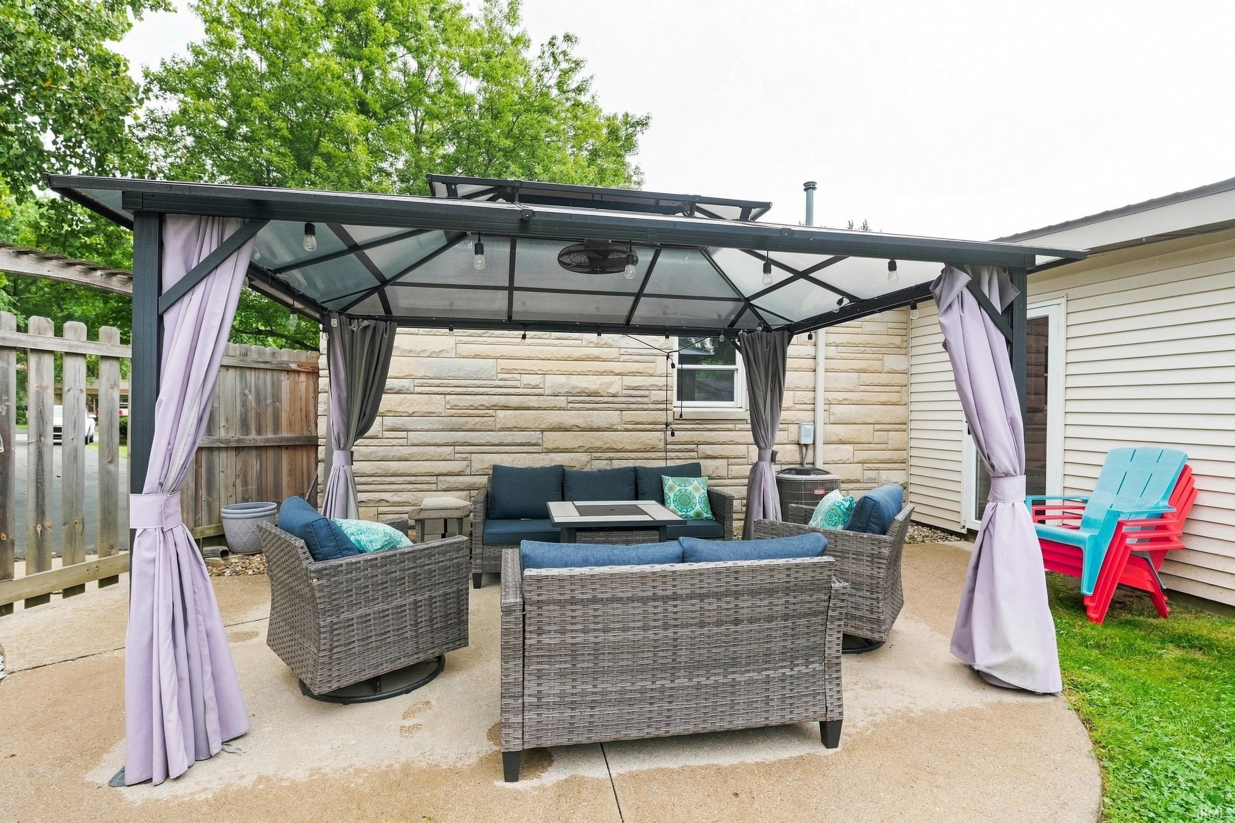 Paved patio featuring a gazebo structure with a hardtop roof and retractable privacy drapes