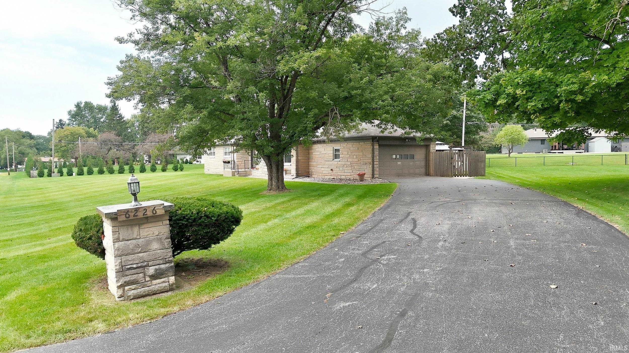 Stone-clad exterior, attached garage, paved driveway, mature trees, manicured lawn, stone mailbox post with integrated lighting