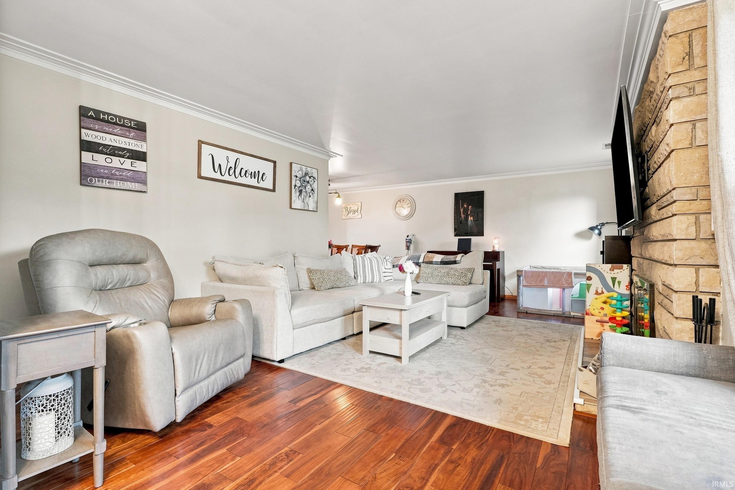 Hardwood-style flooring, crown molding, stone-clad fireplace, recessed lighting, and an open-concept layout
