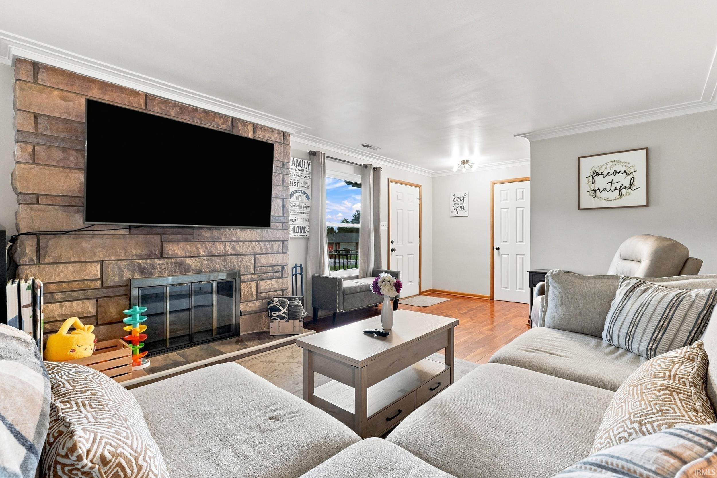 Stone-clad fireplace with a built-in firebox, crown molding, wood-finish flooring, and recessed lighting