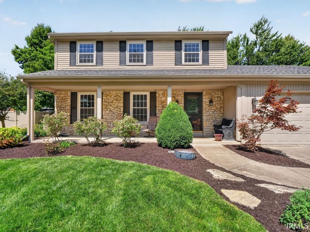 Two-story exterior with stone veneer and horizontal siding, covered front porch with columns, attached garage, concrete pathway, and established landscaping
