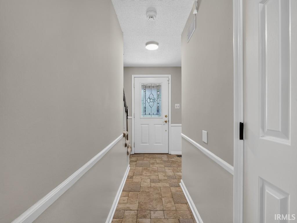 Entryway featuring tile flooring, wainscoting, and a white front door with decorative glass