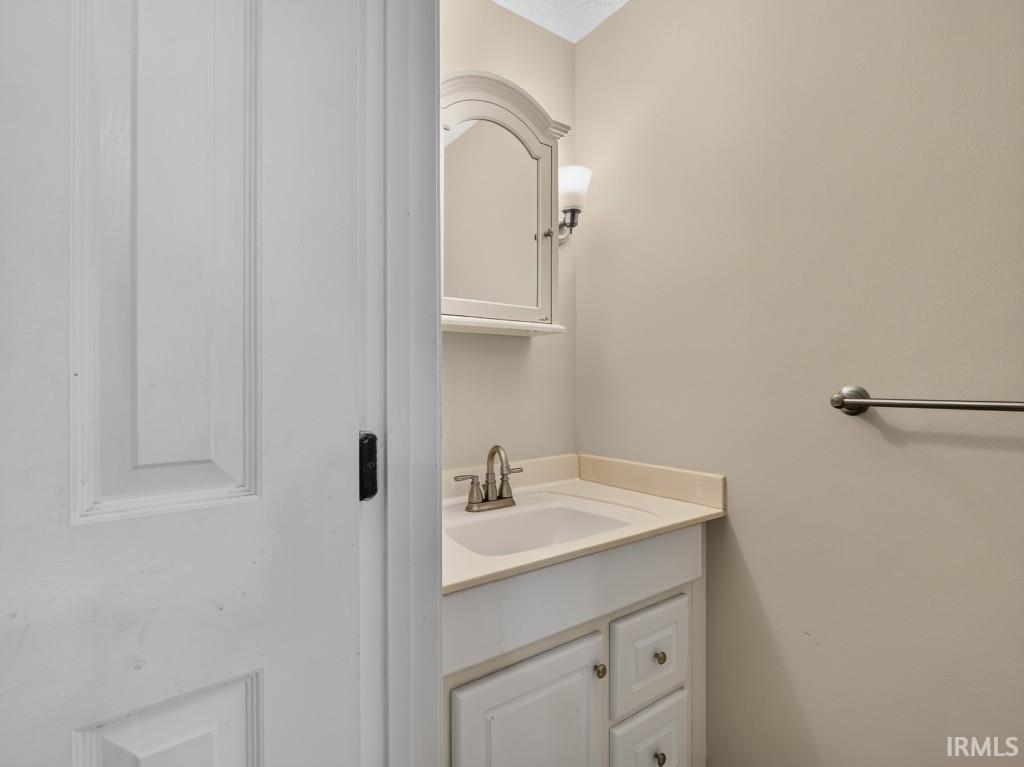 White paneled door with dark hardware, a vanity with an integrated sink and light-toned countertop, a medicine cabinet with an arched mirror, and a wall-mounted light fixture