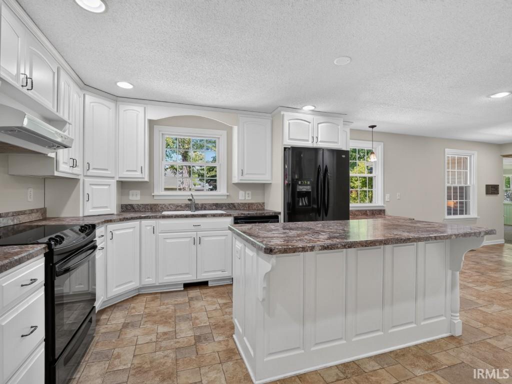 White cabinetry, black appliances, a central island, and patterned tile flooring