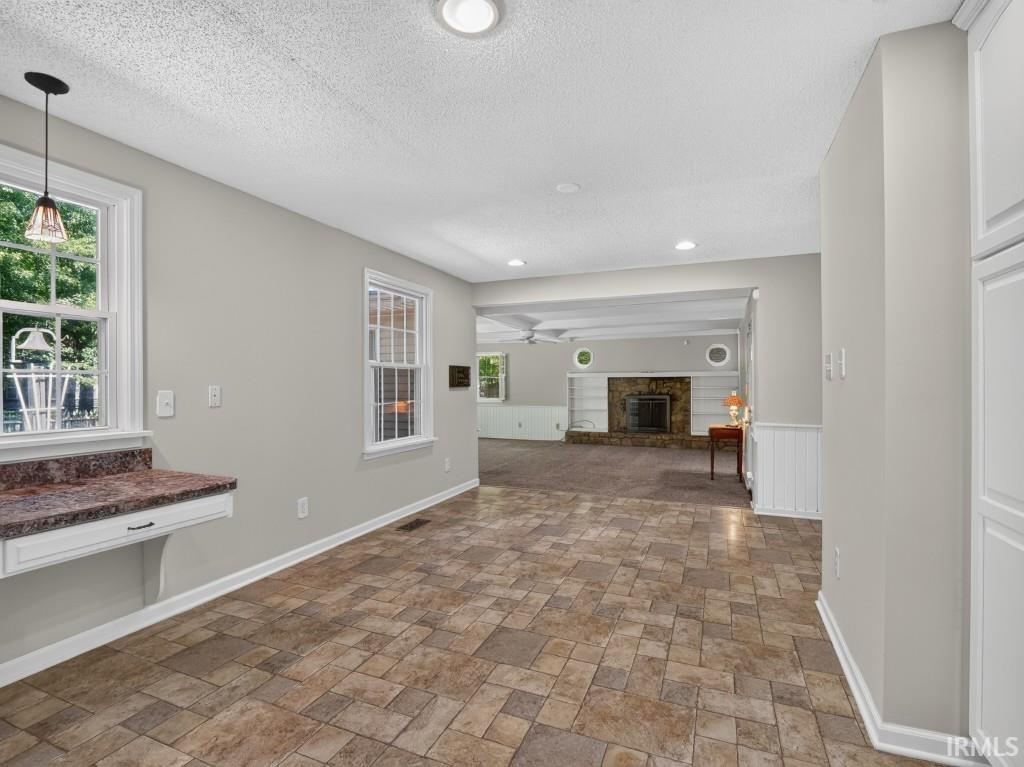 Tile flooring leading to a living area with a stone fireplace, recessed lighting, and white cabinetry