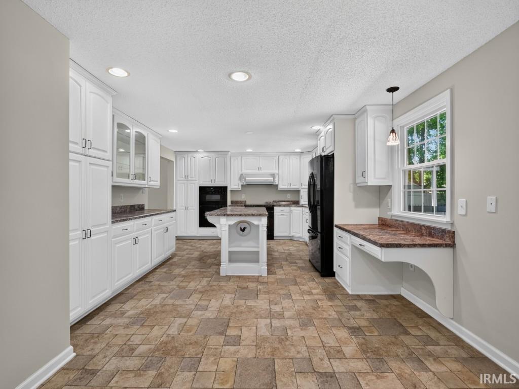 Kitchen featuring extensive white cabinetry, a central island with storage, dark countertops, a built-in oven, and a designated desk area