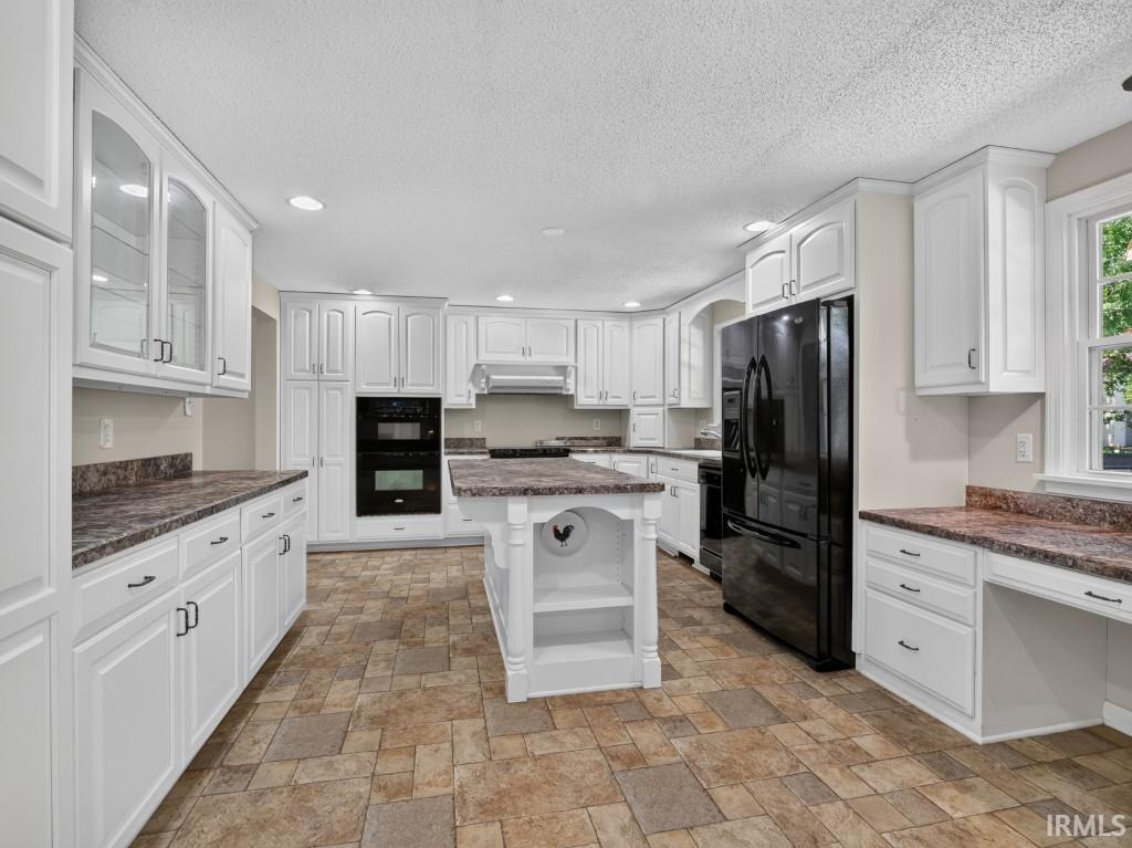 Kitchen featuring white cabinetry, built-in double ovens, a central island, patterned tile flooring, and dark countertops