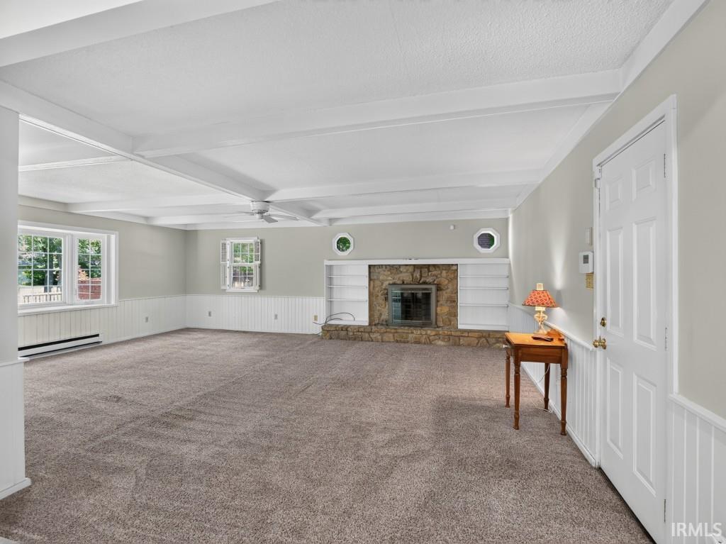 Expansive interior with exposed beam ceiling, stone-surround fireplace, built-in shelving, and beadboard wainscoting