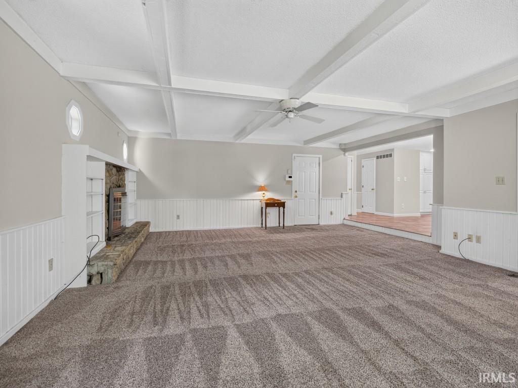 Spacious living area featuring exposed ceiling beams, wainscoting, an integrated stone fireplace, and built-in shelving
