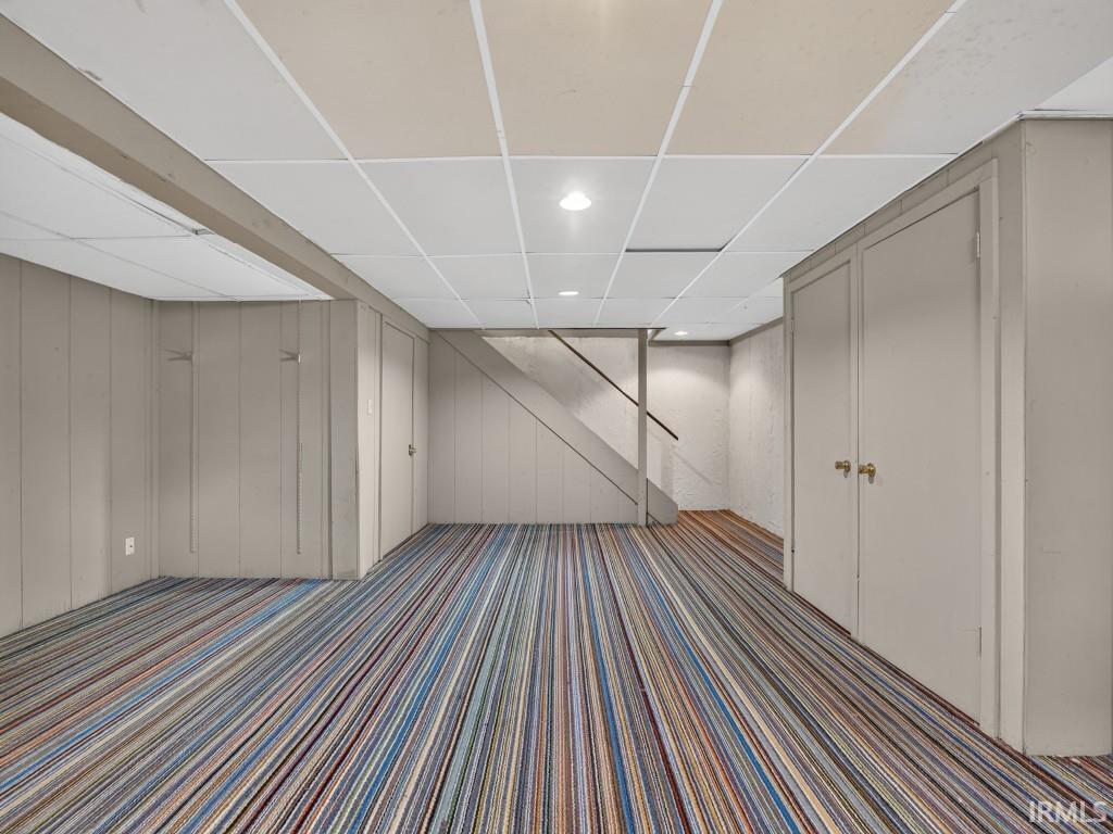 Spacious finished lower level featuring a drop ceiling, recessed lighting, wall paneling, and an interior staircase