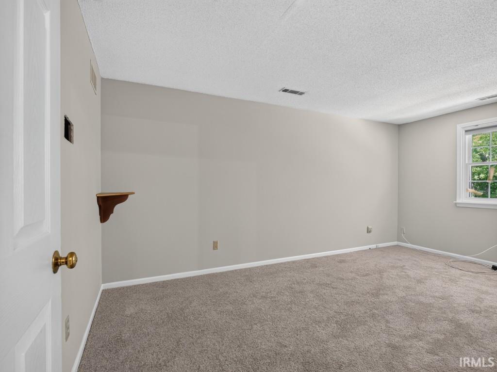 Light gray wall paint, carpeting, window with white trim, white door with brass knob, and wood-finish wall shelf