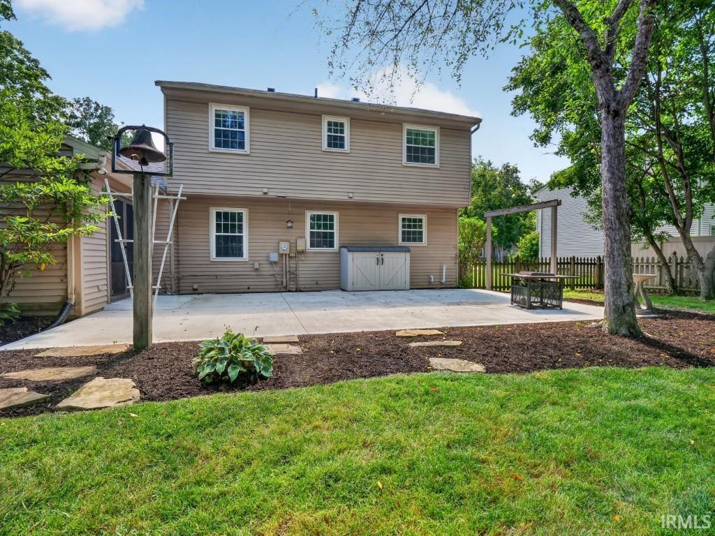 Expansive concrete patio, mature trees, manicured lawn, and wooden privacy fence